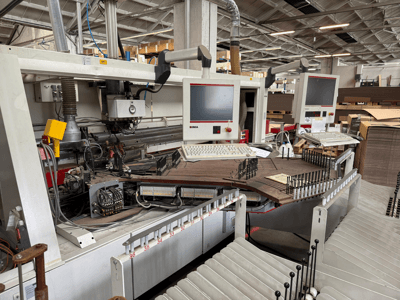 IMA precisiemachine voor houtbewerking met dubbele monitoren en bedieningspanelen, vooraanzicht met transportband en gereedschapsgebied.