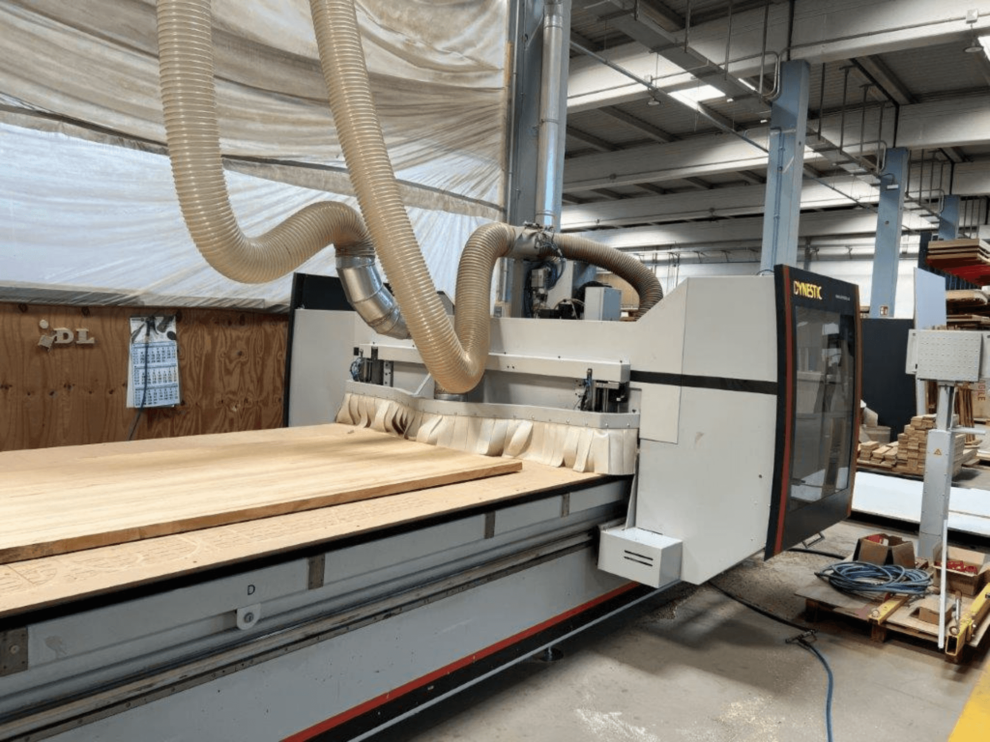 CNC machine van Dynestic, vooraanzicht, met een groot houten werkstuk en stofafzuigslang in een werkplaats.
