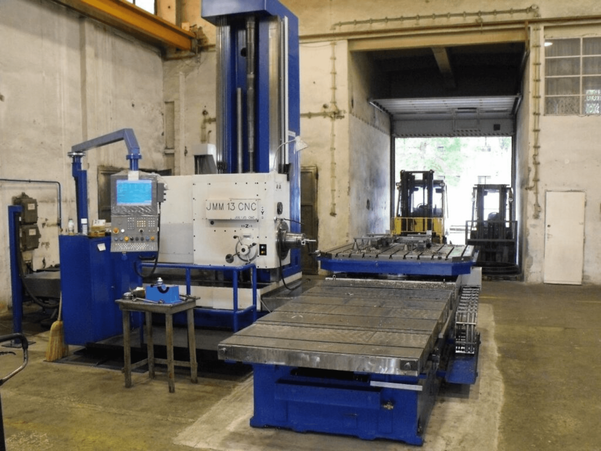 JMM 13 CNC freesmachine in een werkplaats, vooraanzicht, met bedieningspaneel, grote werktafel en industriële achtergrond.