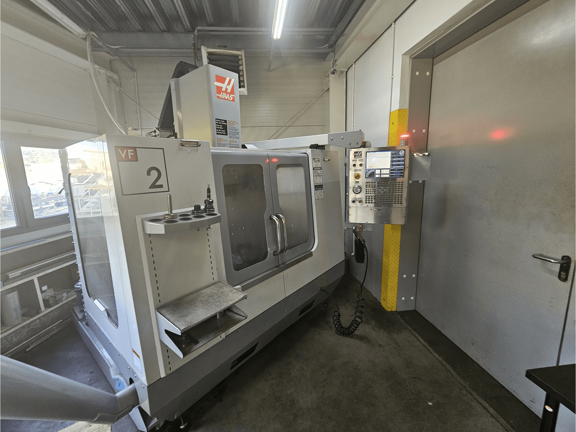 Haas VF-2 CNC freesmachine, vooraanzicht, met bedieningspaneel, gereedschapshouders en een duidelijk venster op de werkruimte.