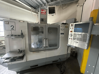 Haas VF-2 CNC machine, vooraanzicht, met bedieningselementen, gereedschapshouder en doorzichtige deuren met zichtbaar gereedschap in de kast.