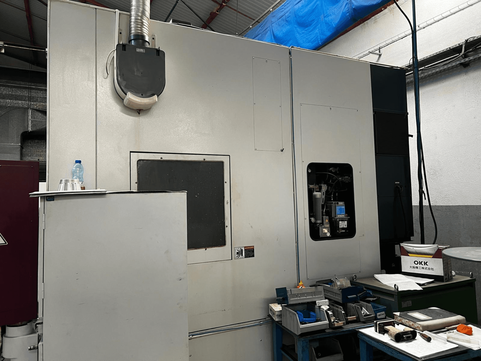 OKK VP600 verticaal bewerkingscentrum in een werkplaats, zijaanzicht met details van de machine en gereedschappen op een tafel ernaast.
