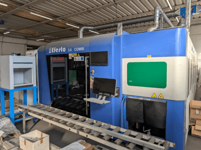 Fiberlasersnijmachine EFESTO 3.6 COMBI, zijaanzicht, met bedieningspaneel en veiligheidsindicatoren, uitgevoerd in een blauwe kleur.