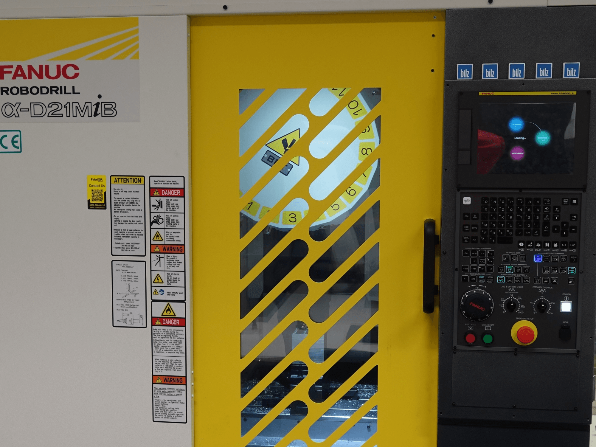 FANUC α-D21MiB verticaal bewerkingscentrum, vooraanzicht, met veiligheidswaarschuwingen, bedieningspaneel en gele veiligheidsdeur.