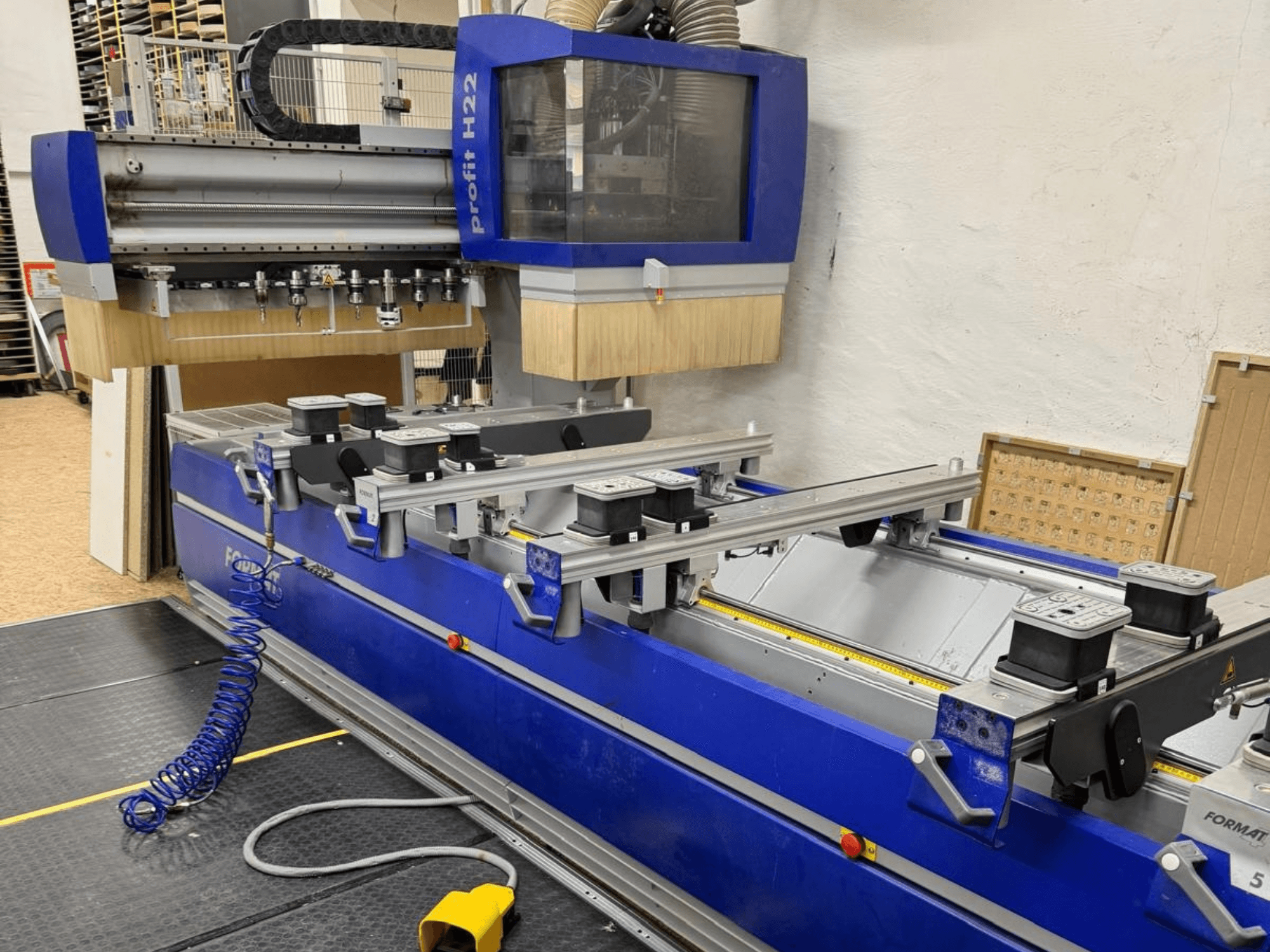 FORMAT4 PROFIT H22 CNC-houtbewerkingscentrum, vooraanzicht, met bewerkingsgereedschappen en spanclips zichtbaar op de blauwe behuizing.
