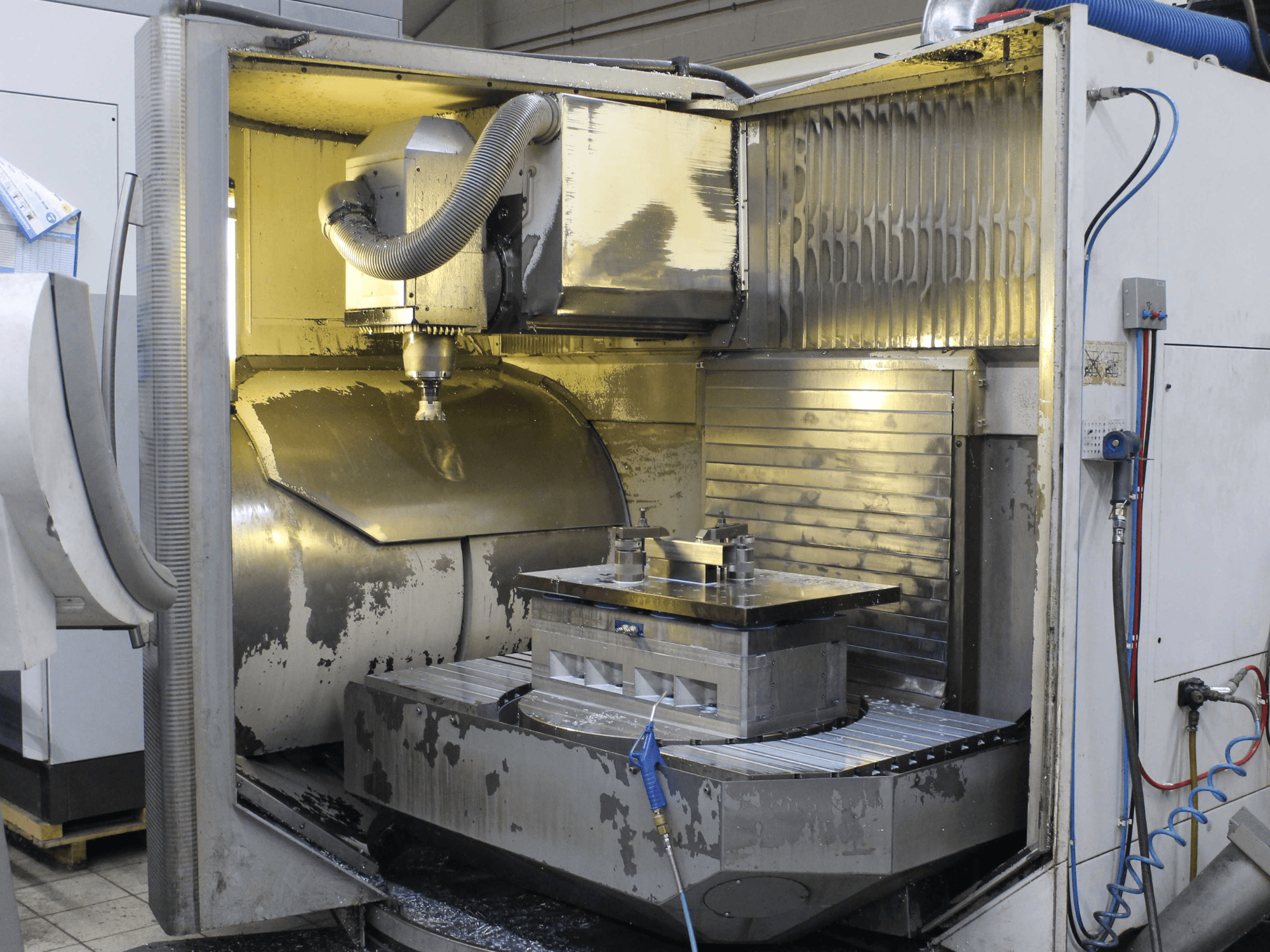 Het interieur van een CNC freesmachine, zijaanzicht, met werkstuk en snijgereedschap met metaalschilfers en koelmiddelresten.