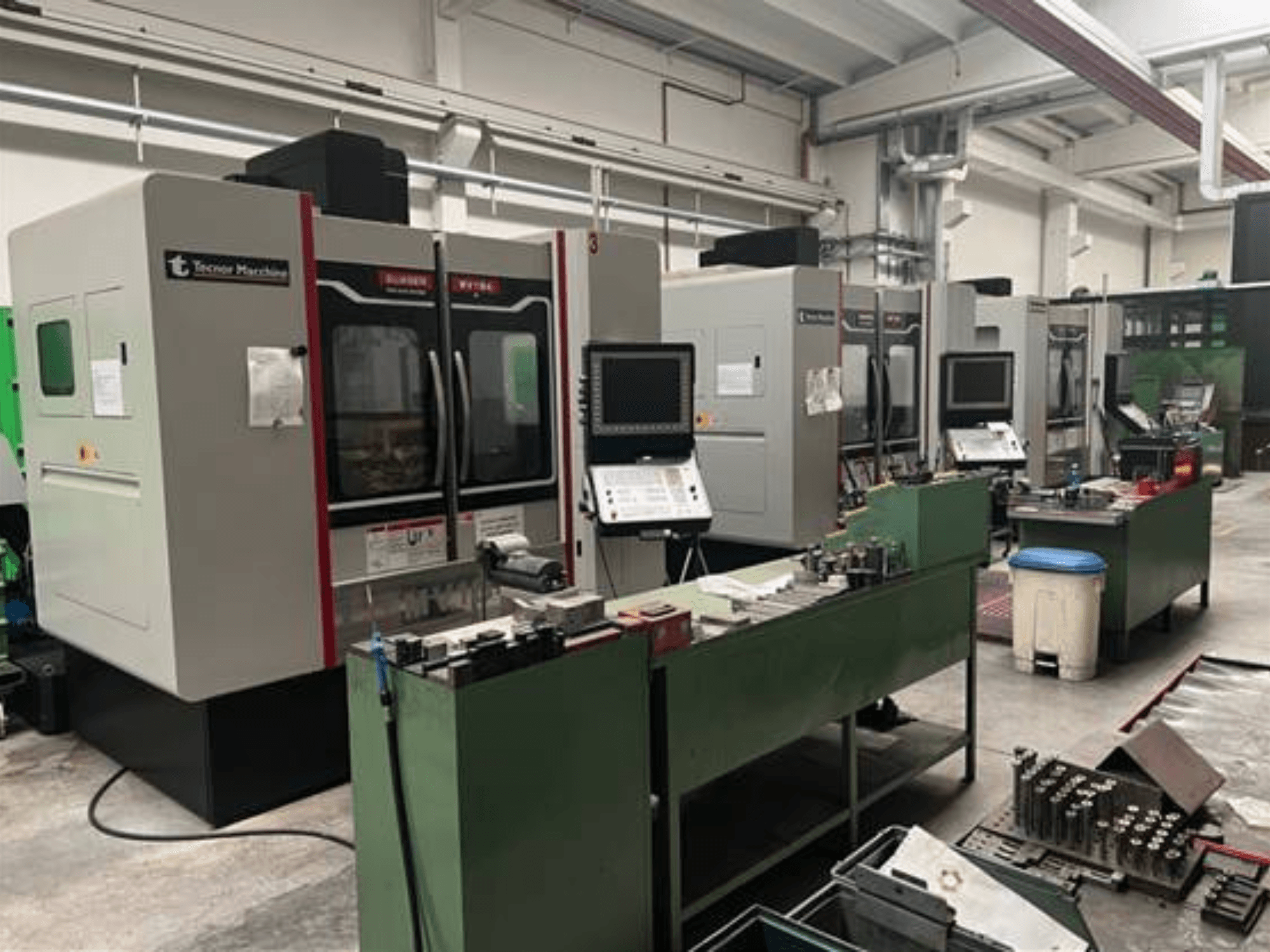 Vier CNC machines van Tecnoer Marchine in een werkplaats, vooraanzicht, met gereedschap en onderdelen op groene werkbanken.