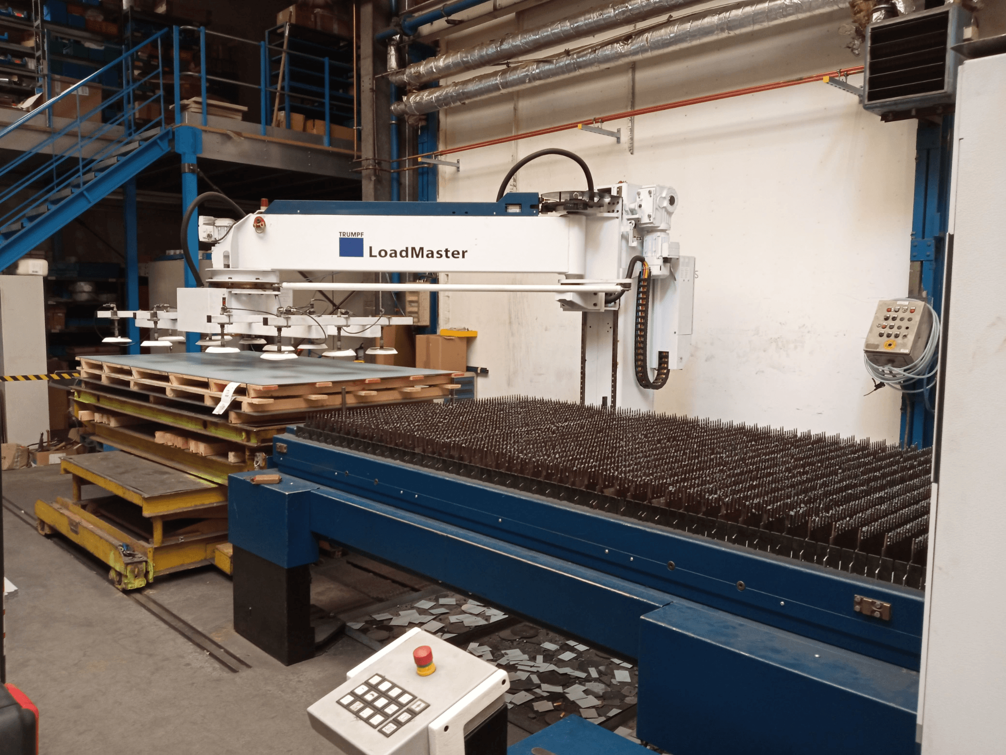 TRUMPF TruLaser 3030 CO₂-lasersnijmachine in zijaanzicht, met een LoadMaster en pallets met materiaal.