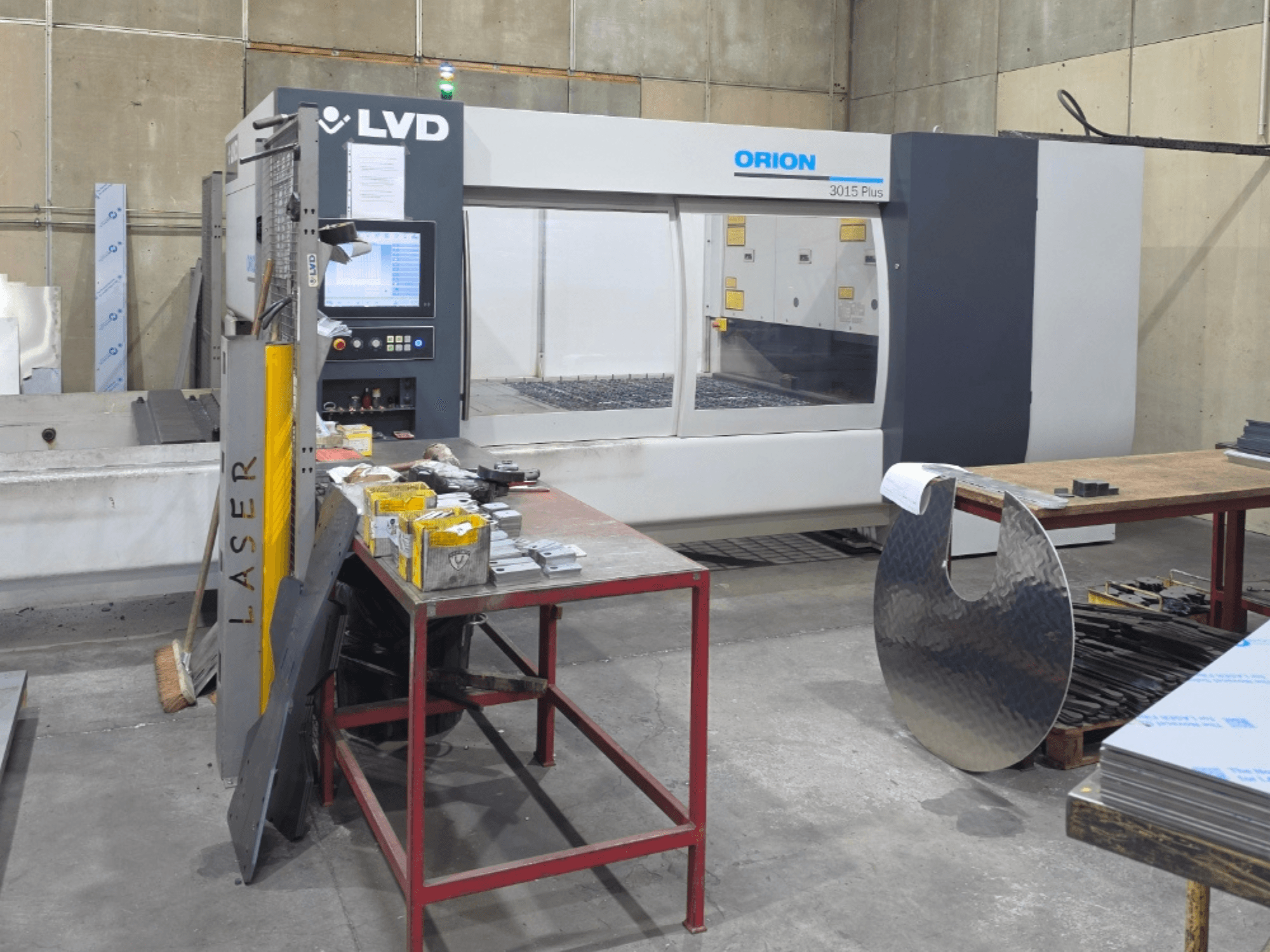 LVD Orion 3015 Plus CO₂-lasersnijmachine, vooraanzicht met bedieningspaneel; omringd door metalen onderdelen op een werktafel.
