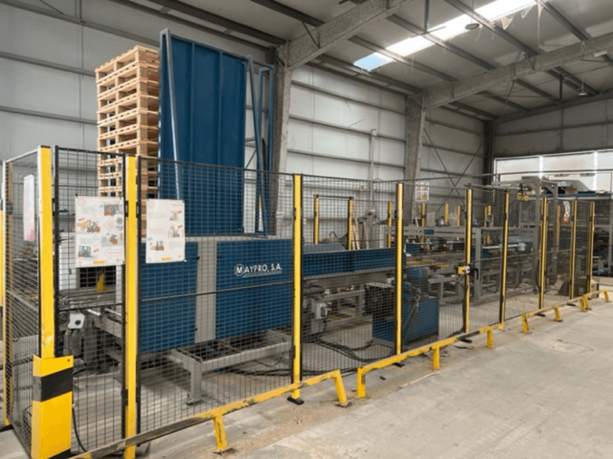 Industriële palletverpakkingsmachine van Maypro S.A. in een magazijn, met veiligheidsnet en bedieningselementen, zijaanzicht.