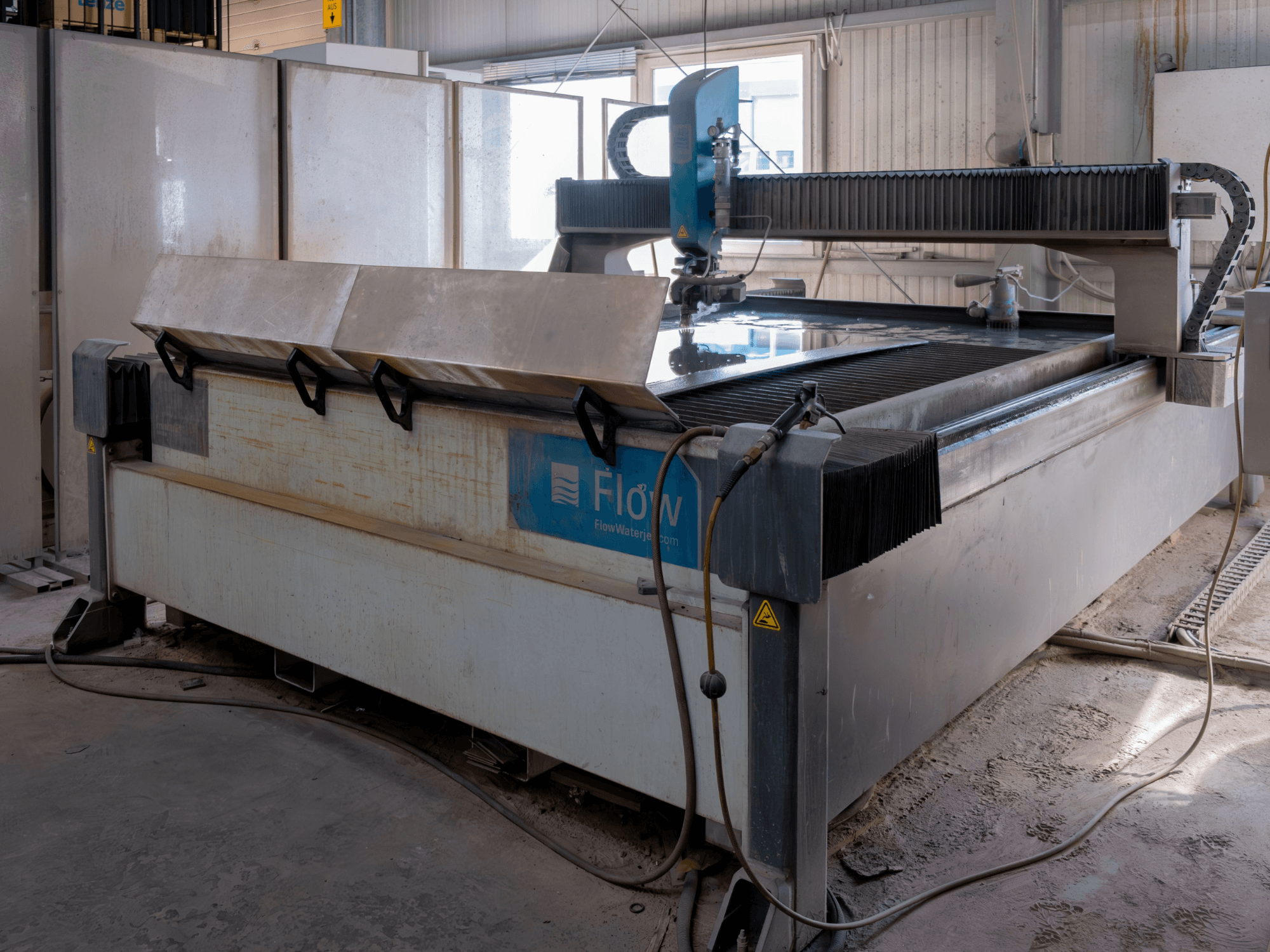 Flow KENT Mach 2 C waterstraalsnijmachine in zijaanzicht, met de roestvrijstalen snijtafel en waterstraalpijp.