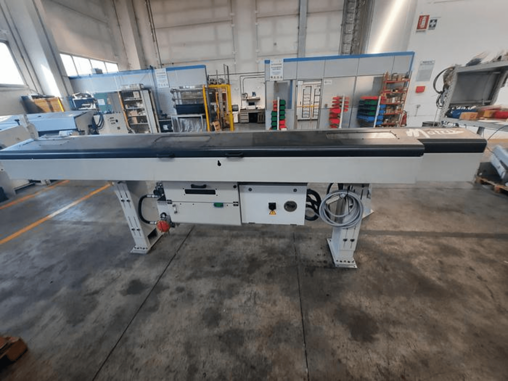 Metalen transporttafel met een glad zwart blad, zijaanzicht, met bedieningsknoppen en kabels; merklogo gedeeltelijk zichtbaar.