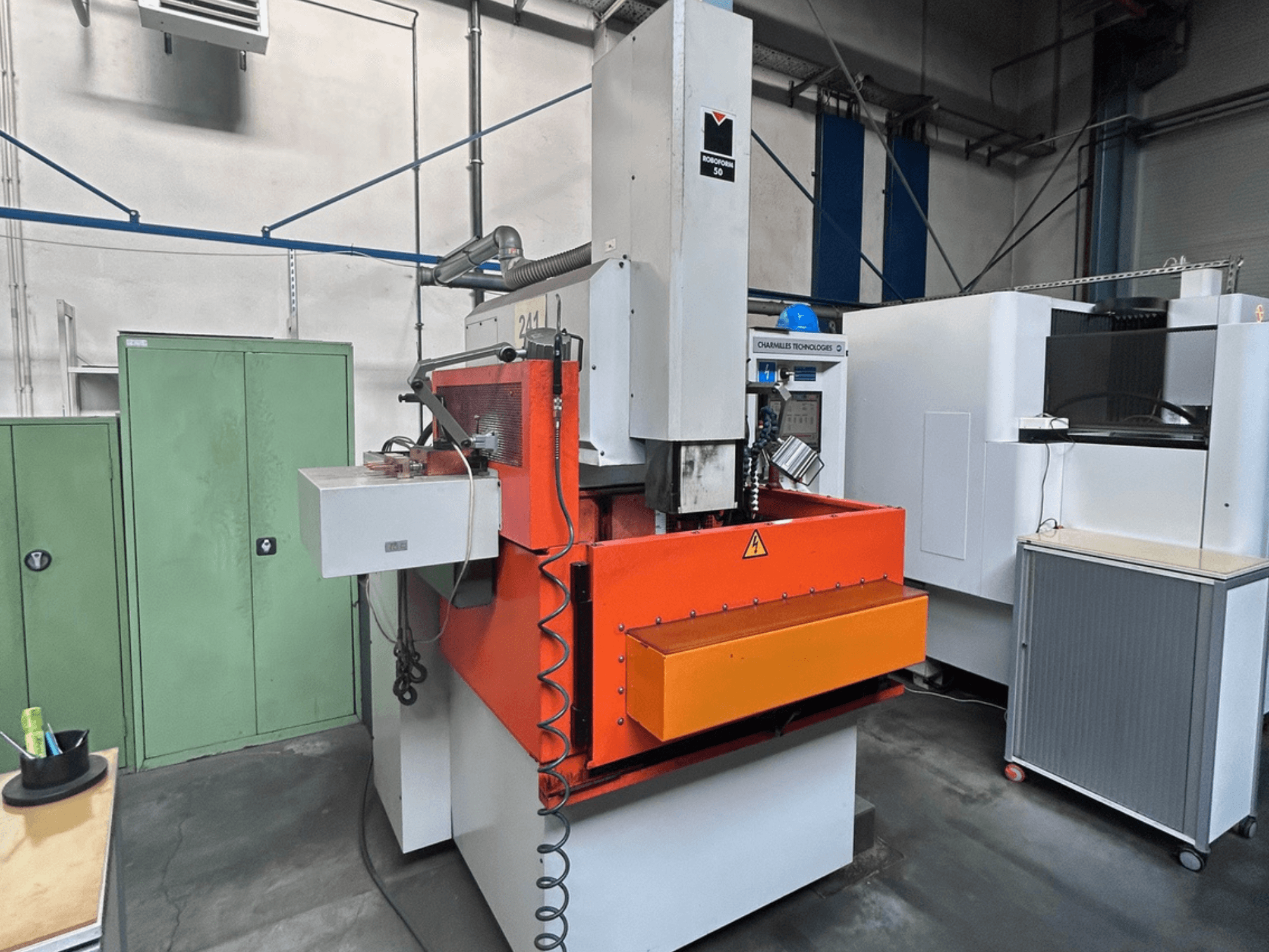 Vooraanzicht van CHARMILLES ROBOFORM 50 zinkvonkmachine met oranje paneel, bedieningsinterface en omringende apparatuur.