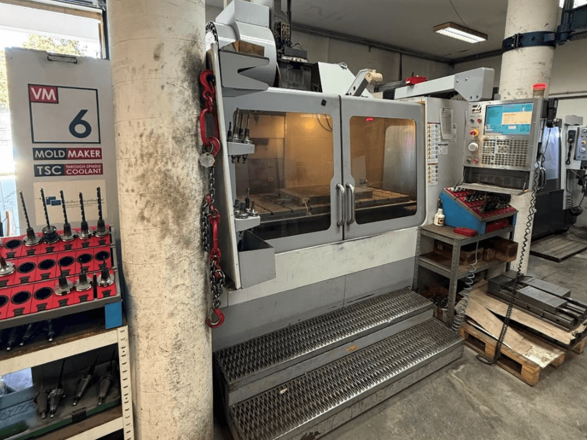 HAAS VM-6 HE verticaal bewerkingscentrum in vooraanzicht, waarbij de bedieningselementen, het koelsysteem en de gereedschapopslag zichtbaar zijn.