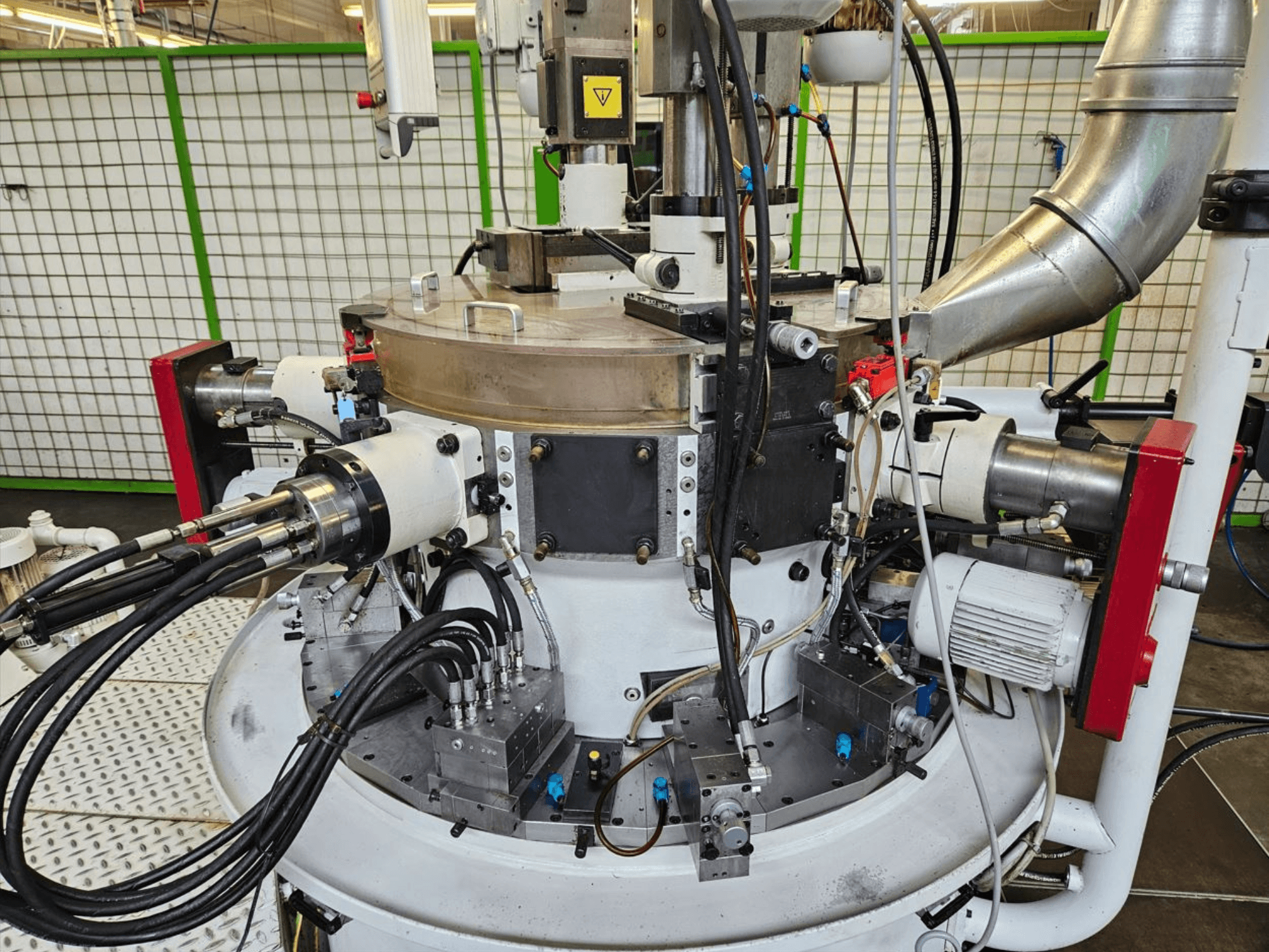 Close-up van een industriële machine met hydraulische slangen, metalen onderdelen en een roterende basis. Geen merk zichtbaar.