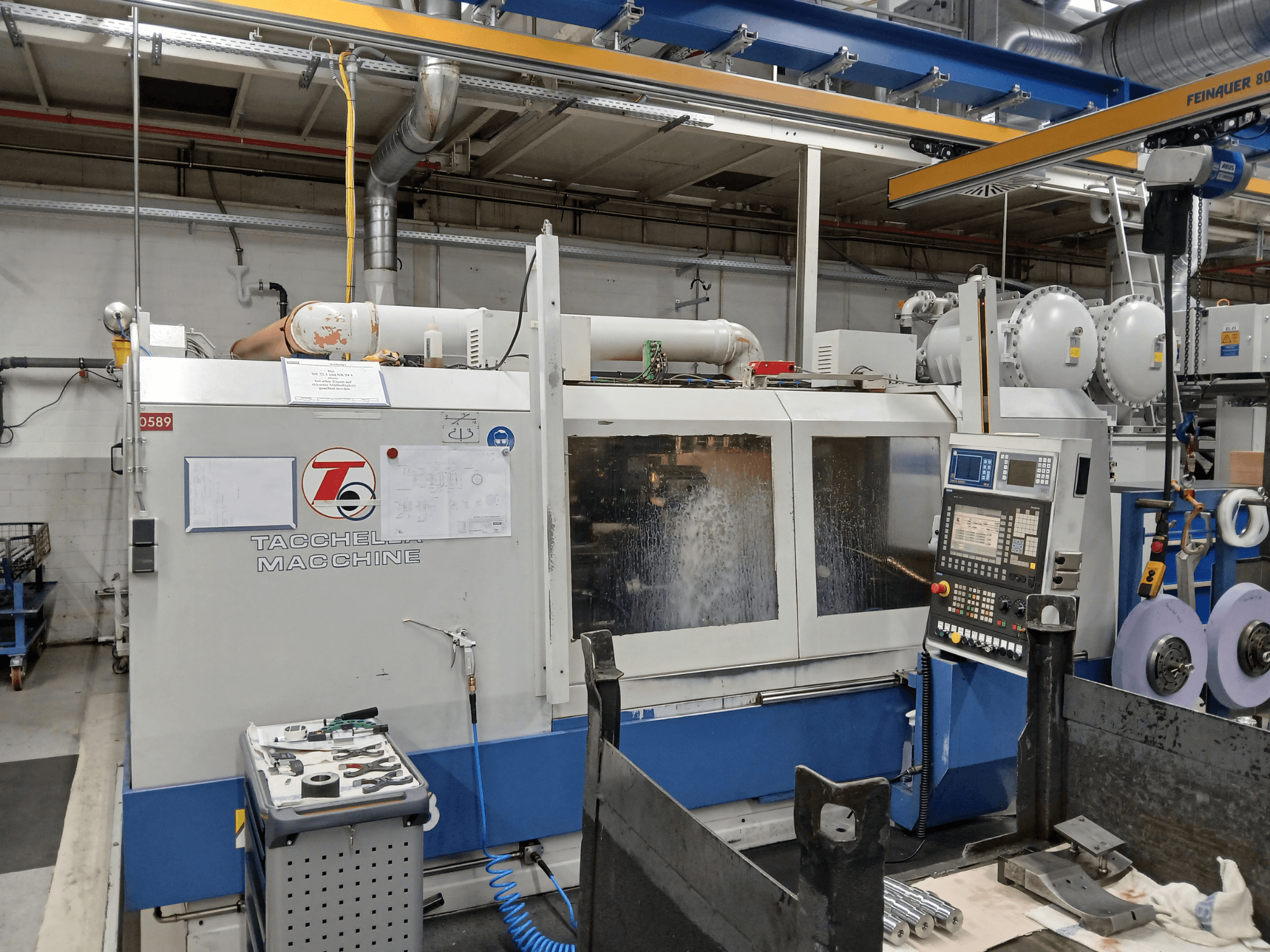 Tacchella bewerkingscentrum in vooraanzicht, met bedieningspaneel en gereedschappen zichtbaar. Waterkoelmiddel spuit tijdens bedrijf.