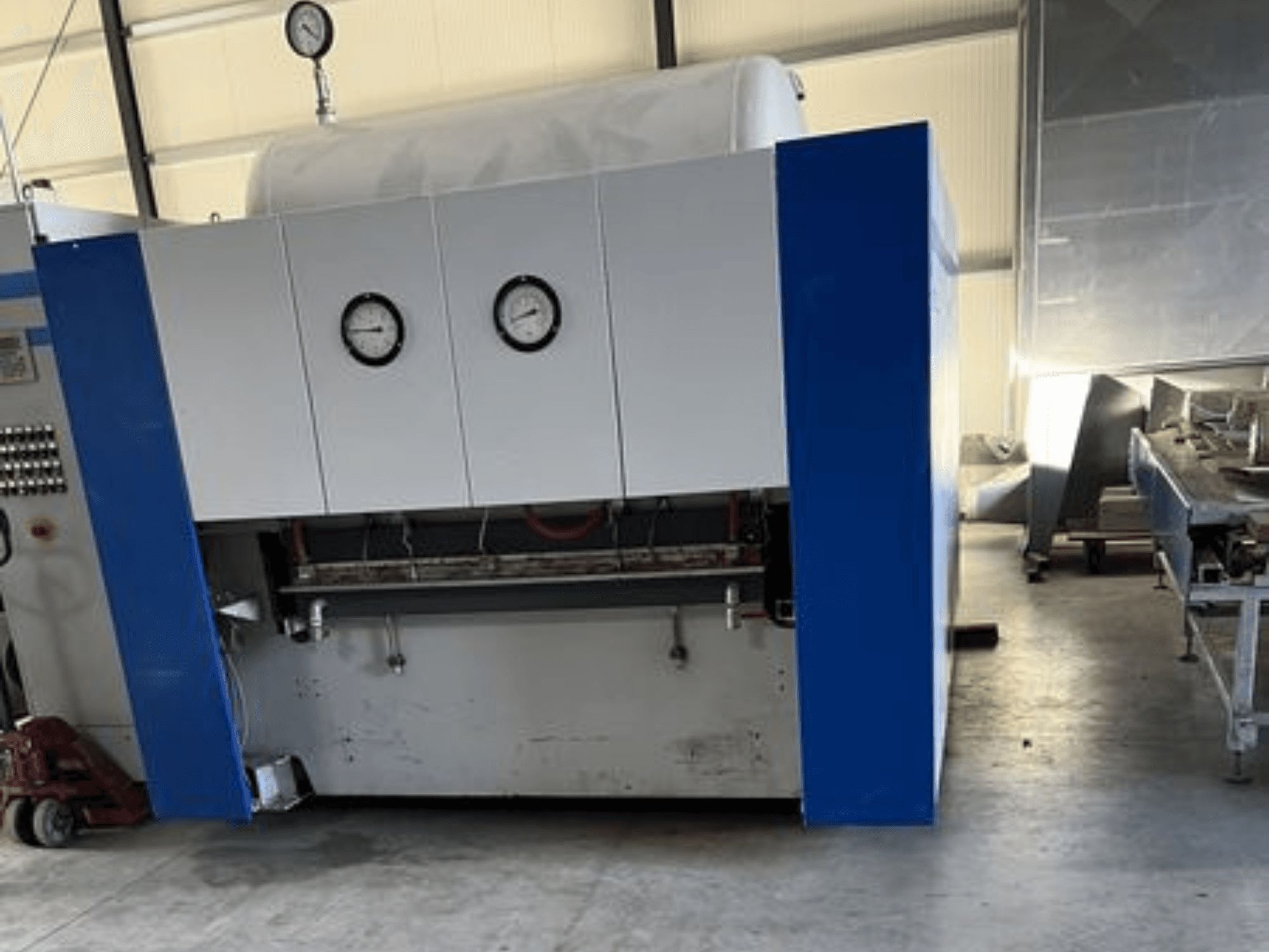 Blauw-witte industriële machine met twee drukmeters, vooraanzicht, met een bedieningspaneel en aangrenzende apparatuur.