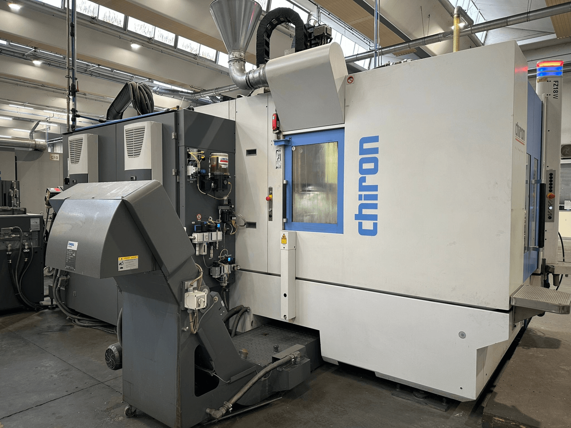 Chiron CNC machine in grijs en wit, vooraanzicht, met bedieningselementen, leidingen en een stofafzuigkap.