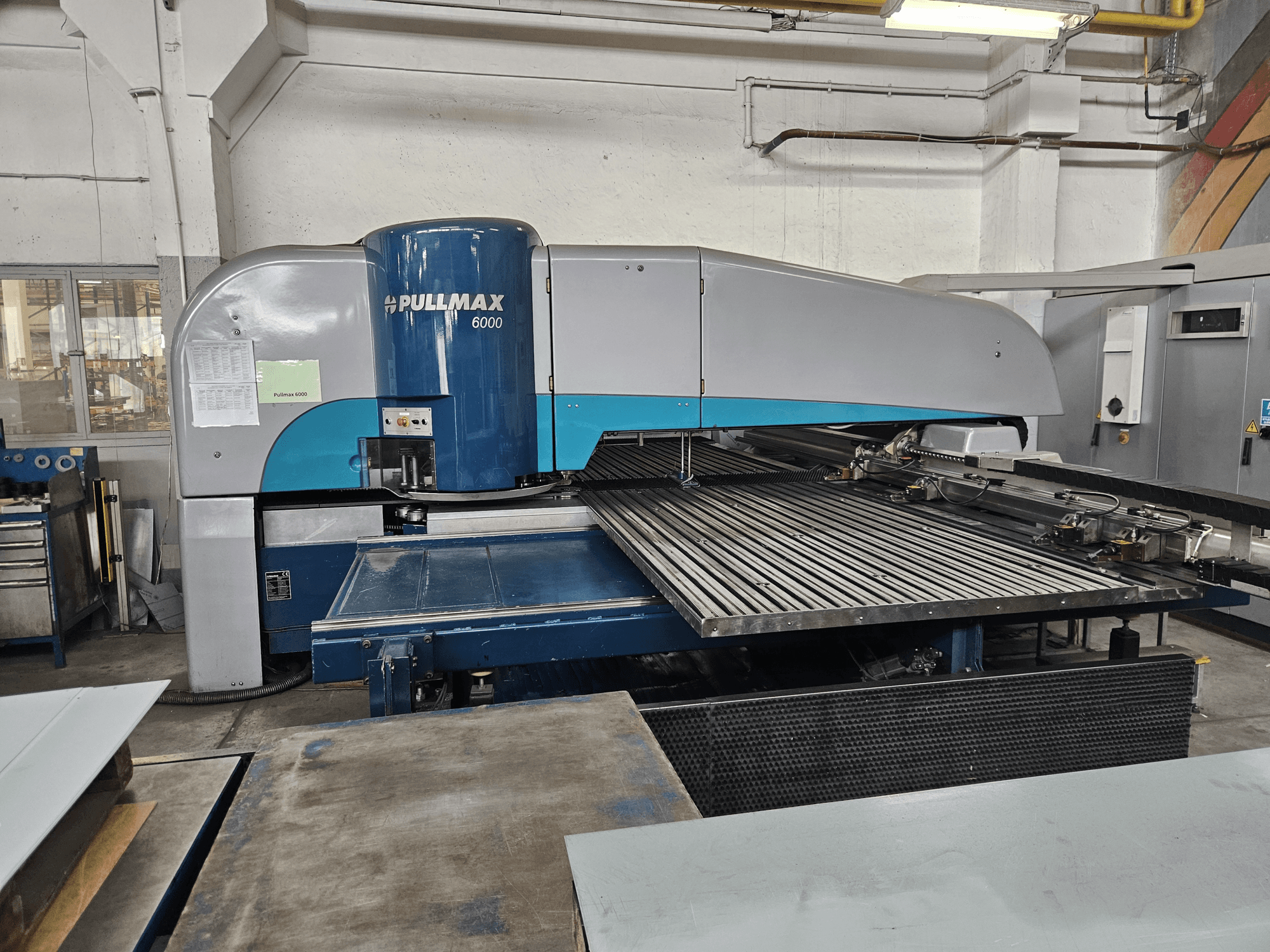 Vooraanzicht van de Pullmax 6000 CNC-ponsmachine, met zijn grote vlakbed en metalen frame in een werkplaatsomgeving.
