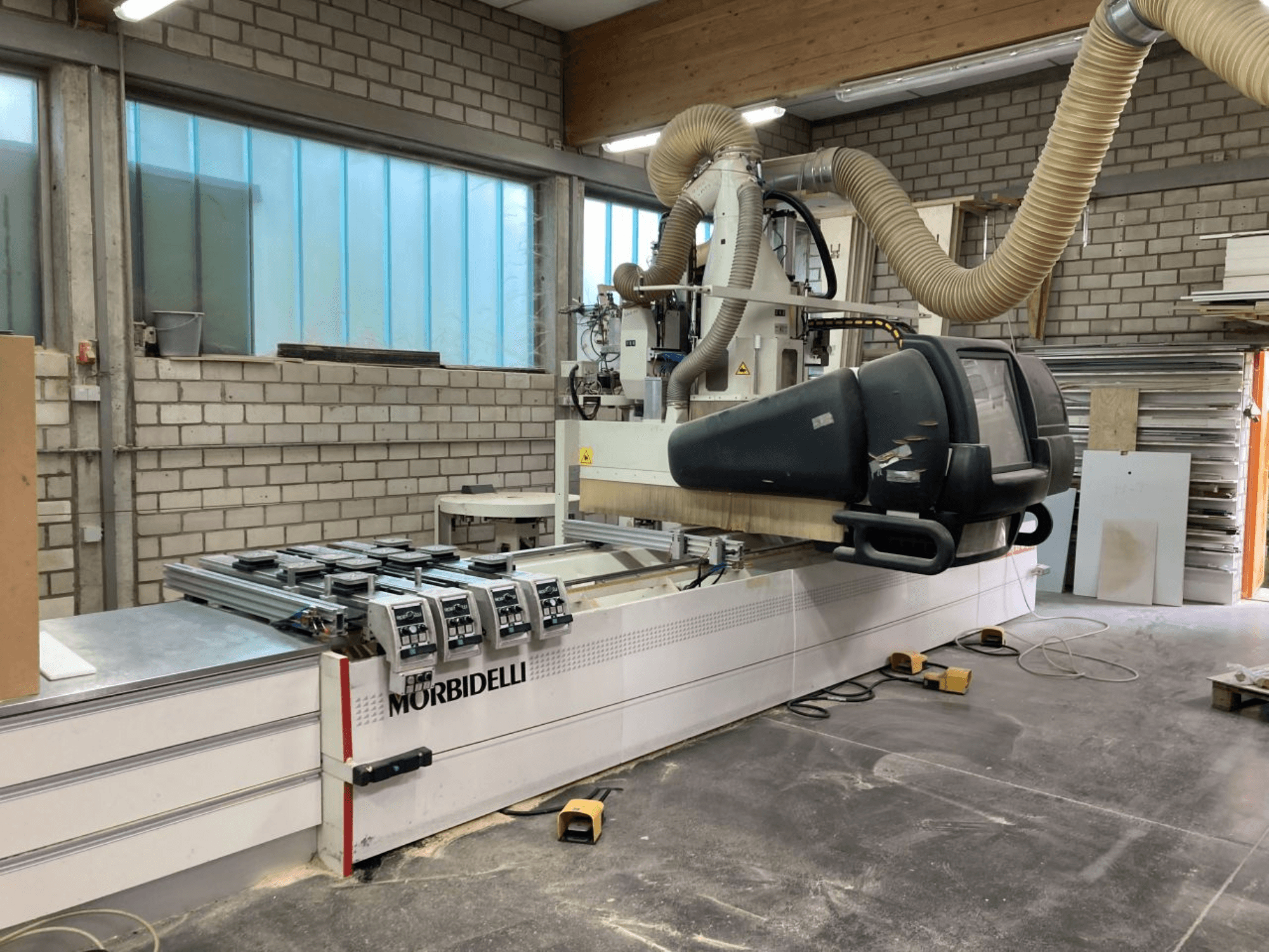 MORBIDELLI CNC machine in een werkplaats, vooraanzicht met bedieningspaneel, stofafzuiging en gepositioneerd houtstuk.