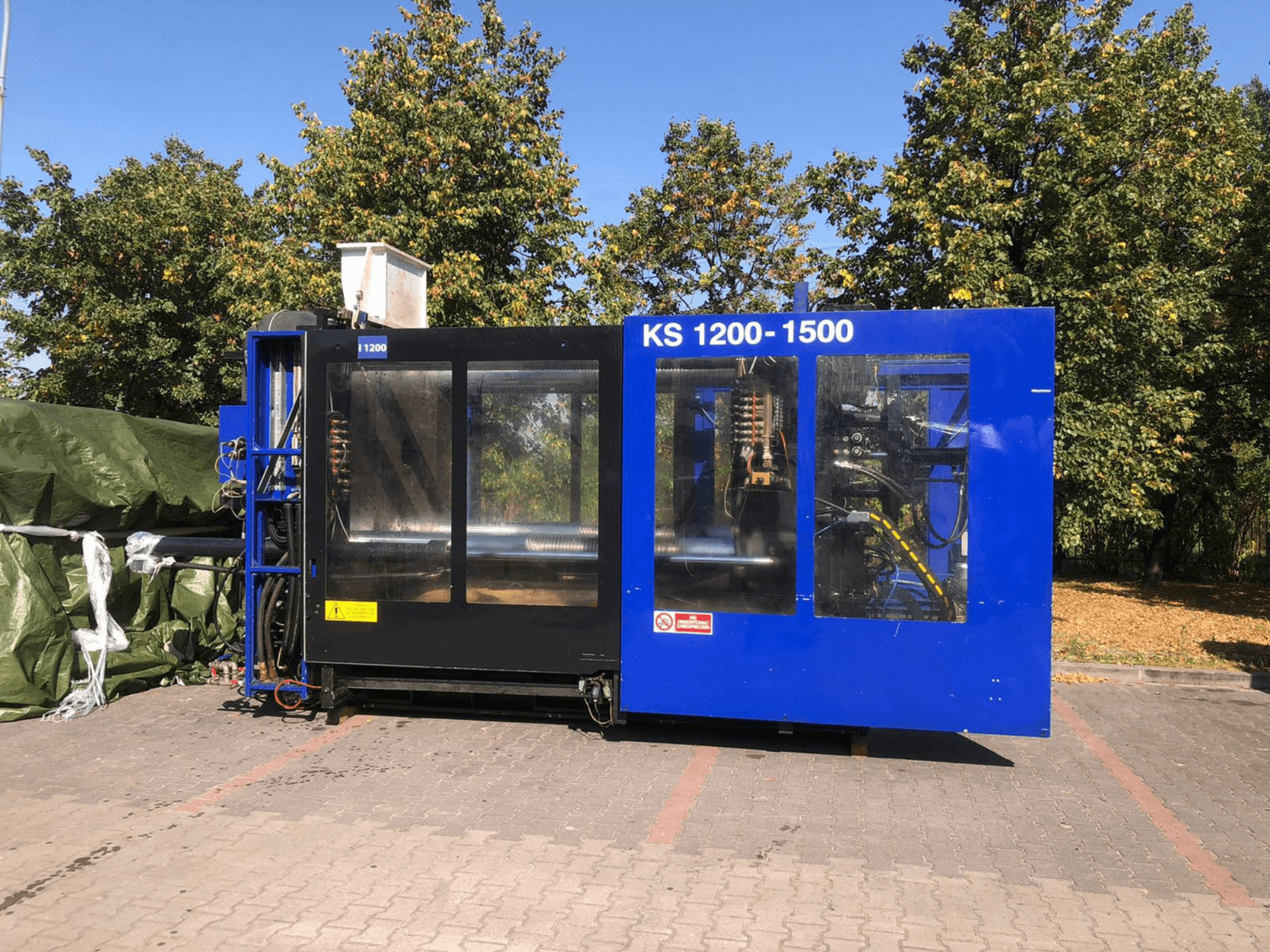 Hydraulische spuitgietmachine ITALTECH KS 1200 8300 ES, zijaanzicht, met bedieningselementen en machinedetails in een parkomgeving.