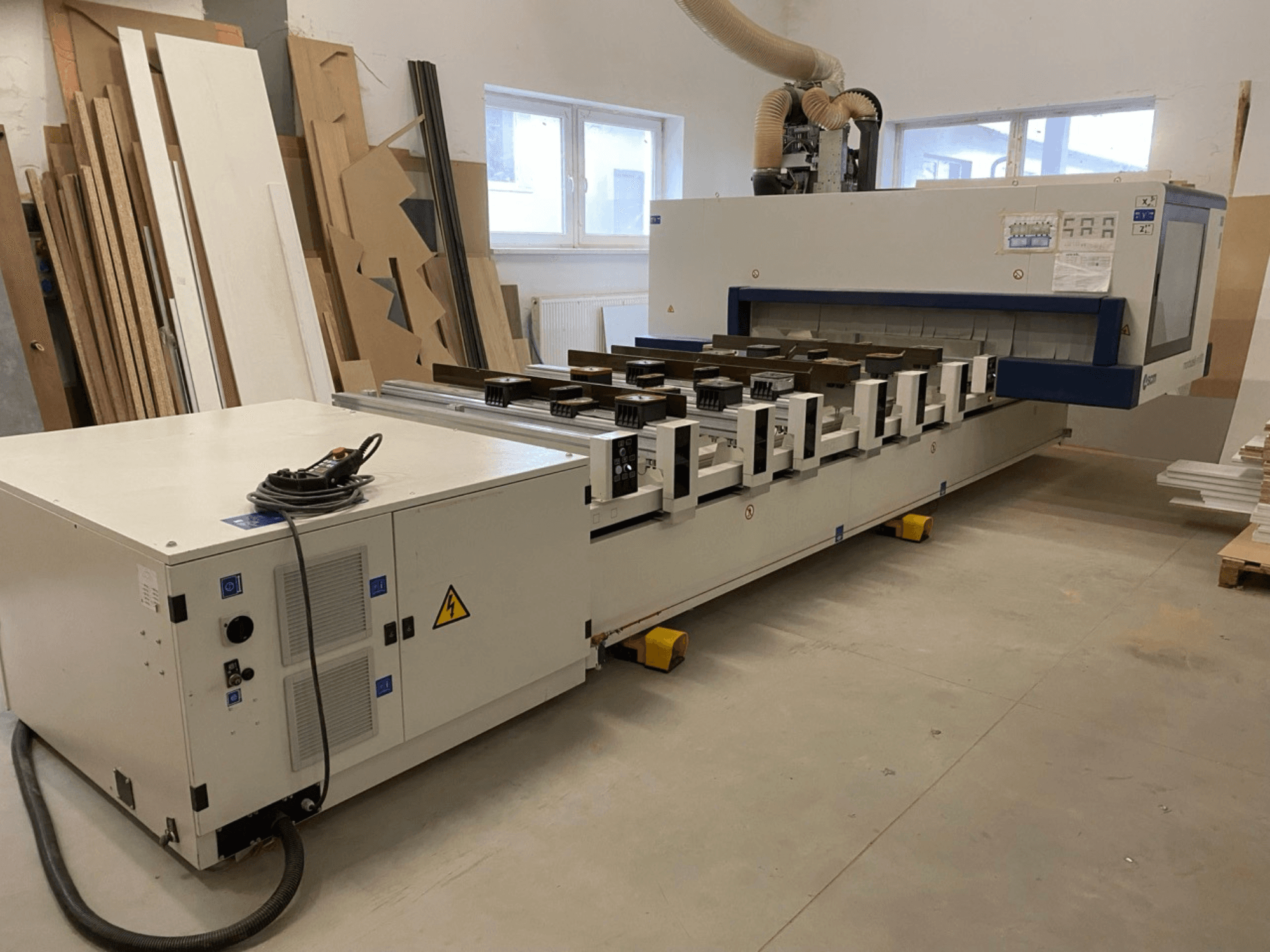 SCM Morbidelli: foto van het M100 CNC-houtbewerkingscentrum in een werkplaats, met een vooraanzicht van het bedieningspaneel en de stofafzuiging.
