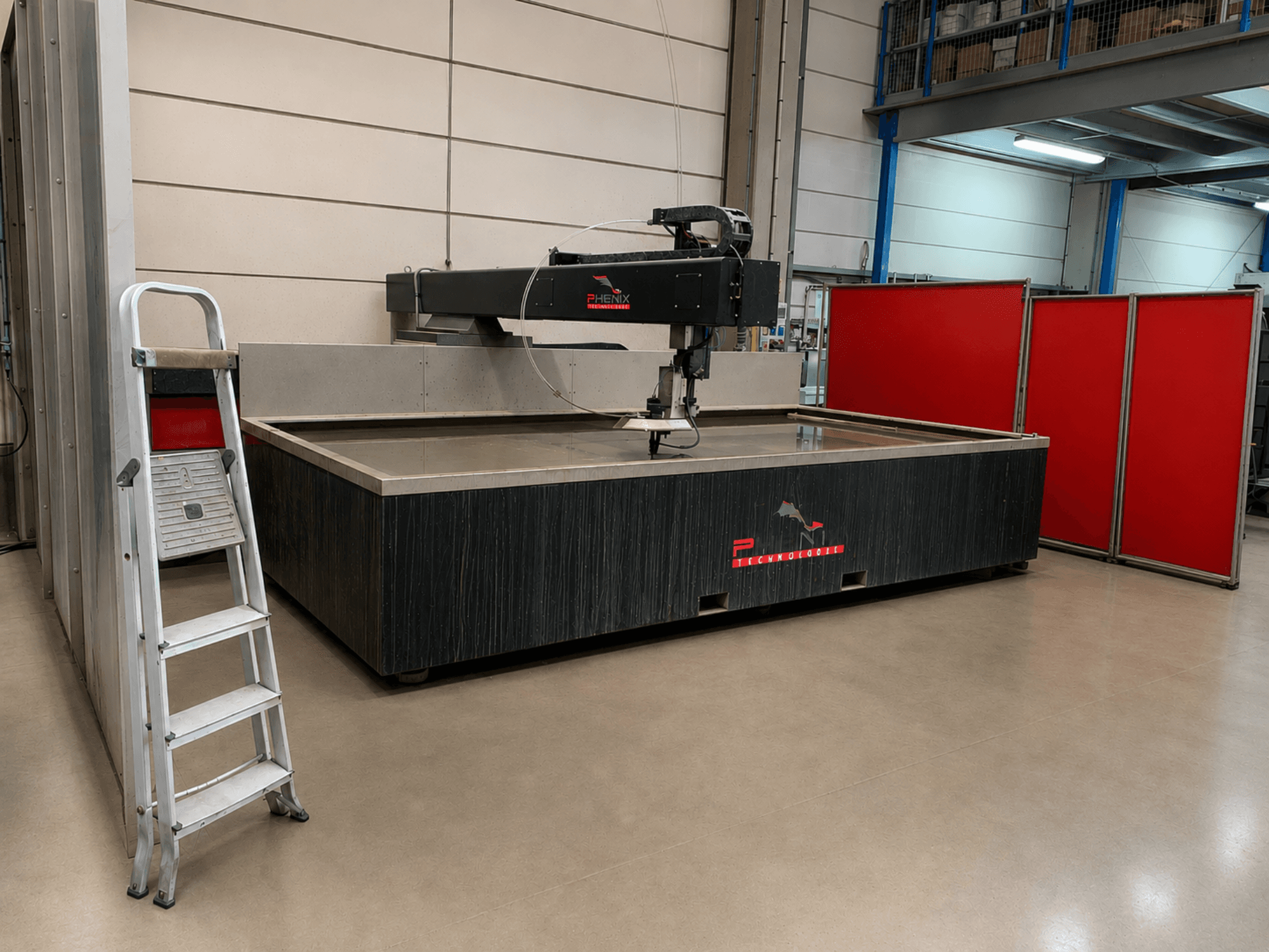 PHENIX TECHNOLOGIE MD-JET 2040 waterstraalsnijmachine in zijaanzicht, met daarnaast een zilverkleurige ladder en rode scheidingspanelen.