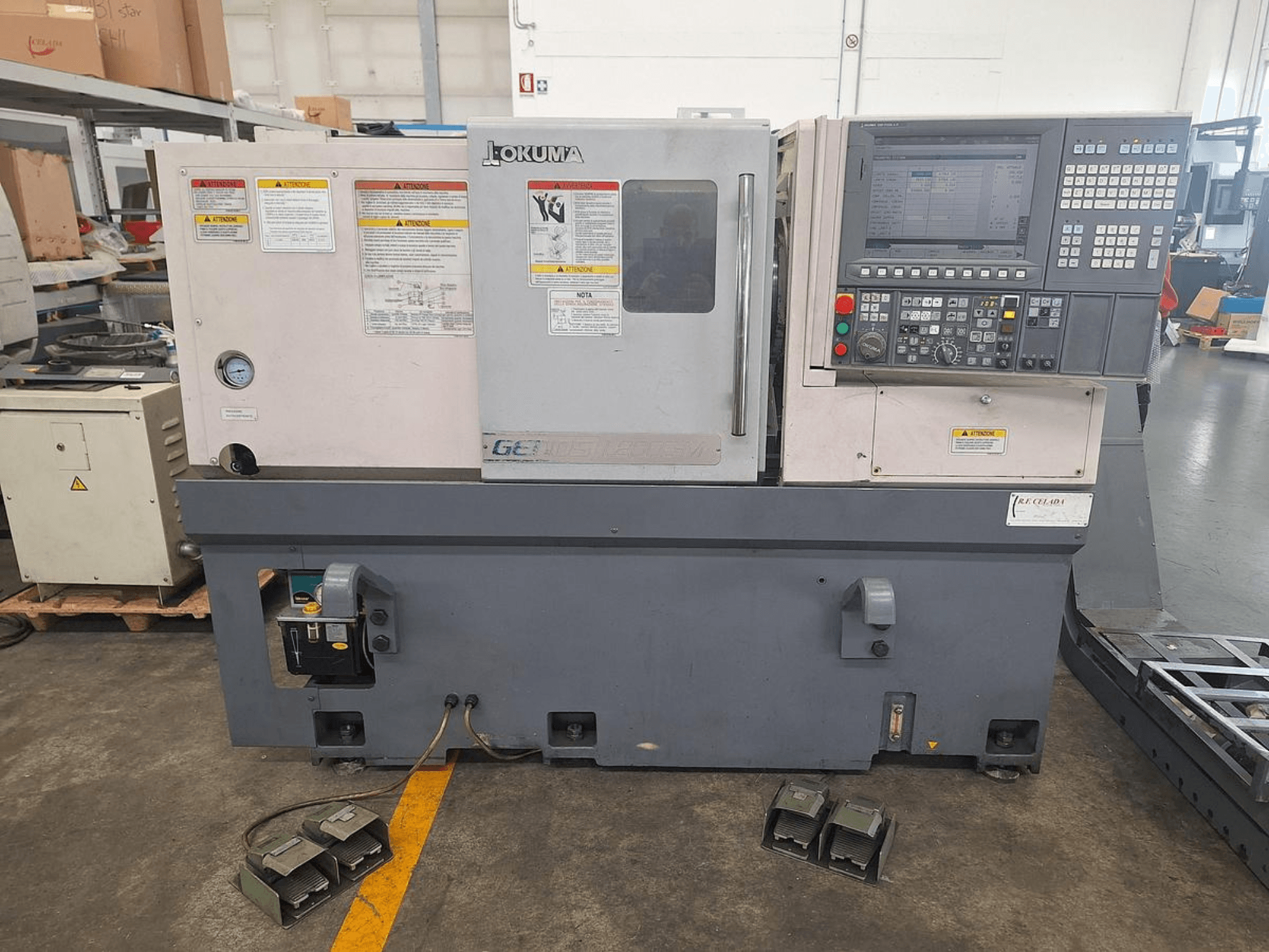 Okuma GENOS L200E-M horizontale draaimachine in zijaanzicht; voorzien van bedieningspaneel, veiligheidswaarschuwingen en voetpedalen.
