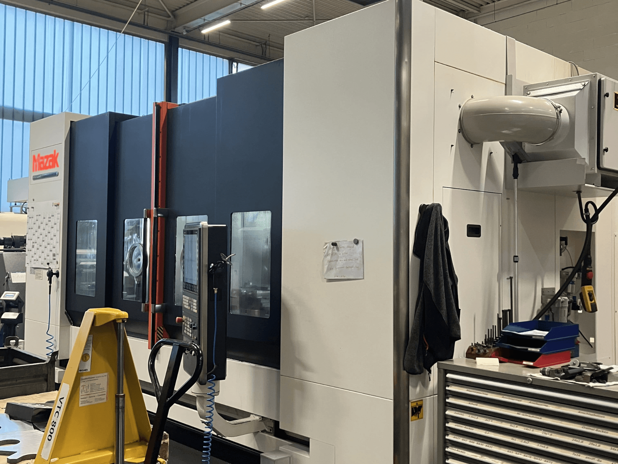 Mazak CNC machine gezien vanaf de zijkant, met het bedieningspaneel en de veiligheidsfuncties in een werkplaats.