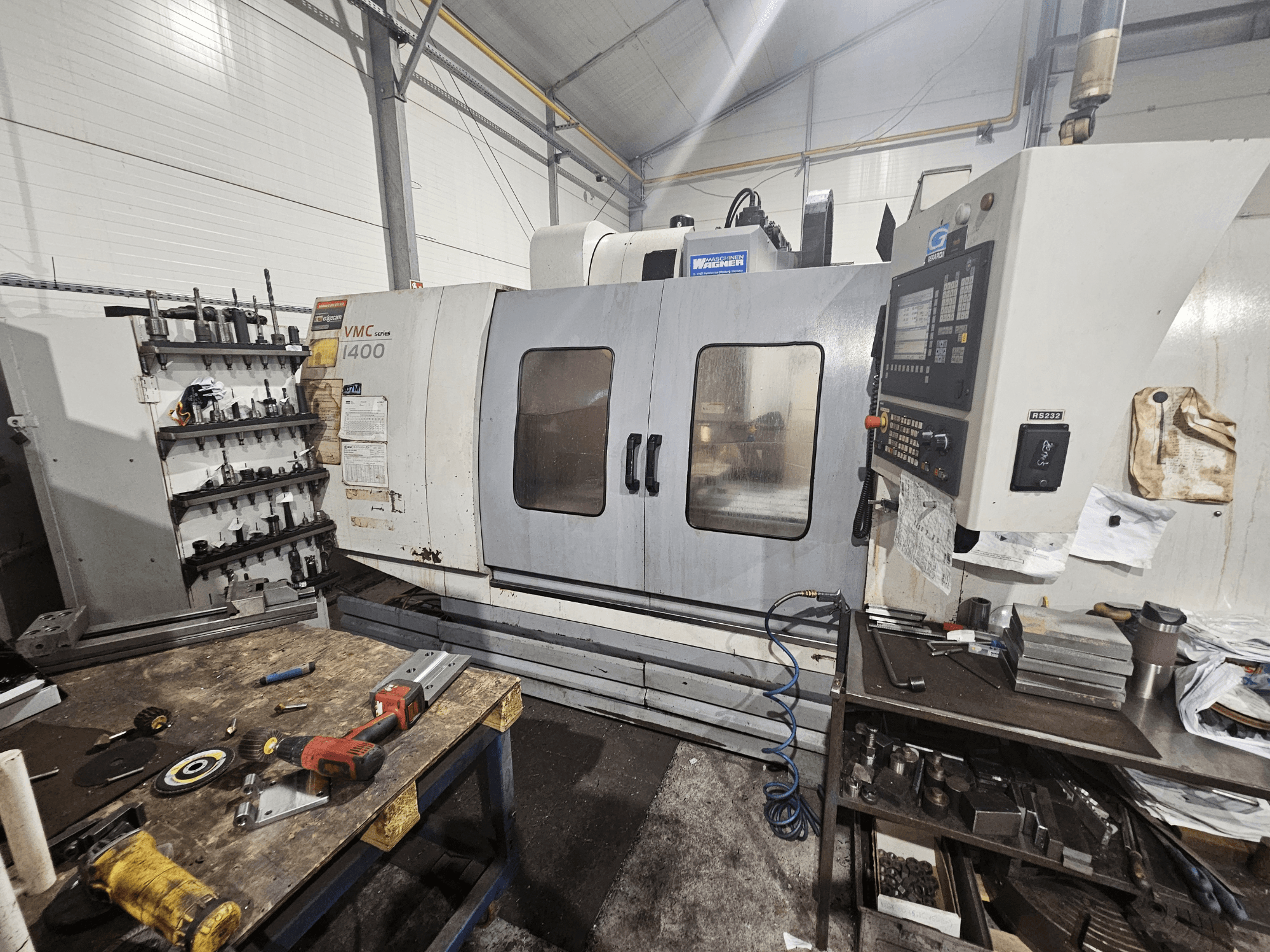 VMC 1400 CNC freesmachine in een werkplaats, vooraanzicht; gereedschap en materiaal verspreid op de werkbank vlakbij.