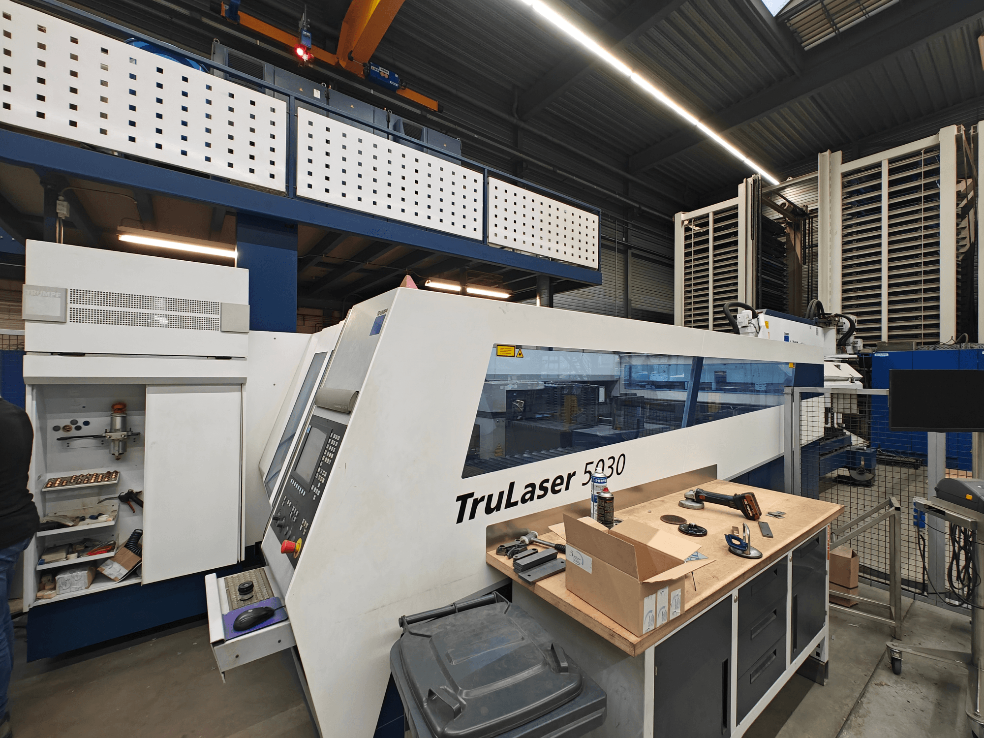TruLaser 5030 machine in een werkplaats, vooraanzicht met bedieningspaneel zichtbaar, omringd door gereedschap en apparatuur.