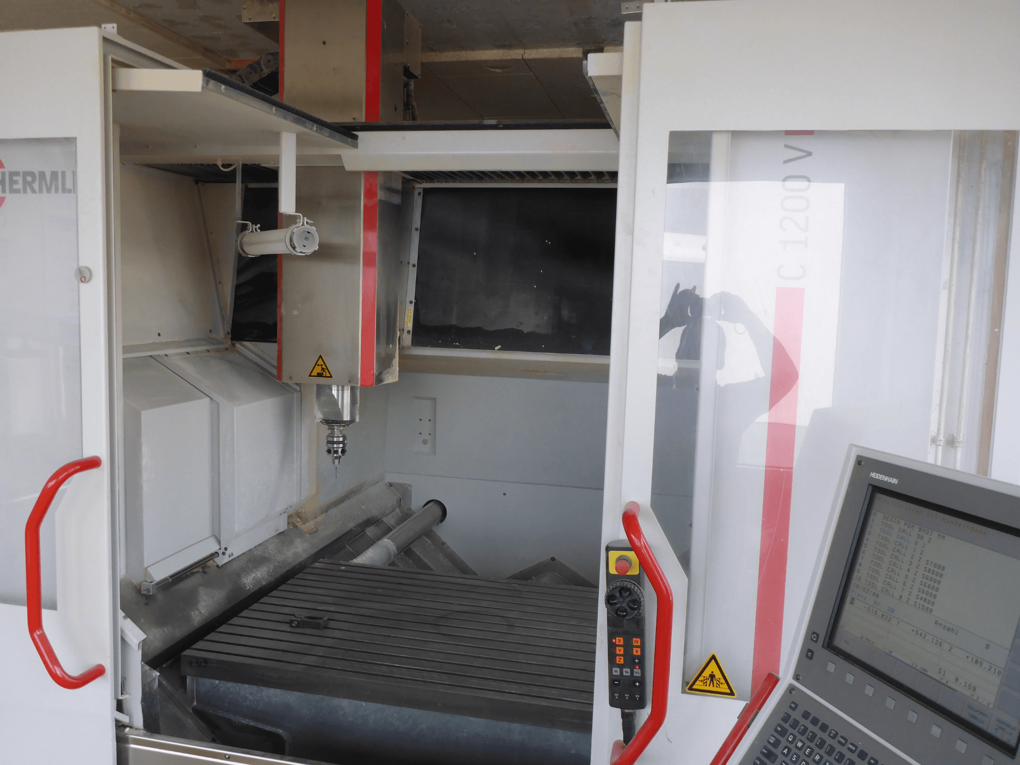 Het interieur van het HERMLE C 1200 verticaal bewerkingscentrum toont de gereedschaphouder, het bedieningspaneel en de werktafel in vooraanzicht.