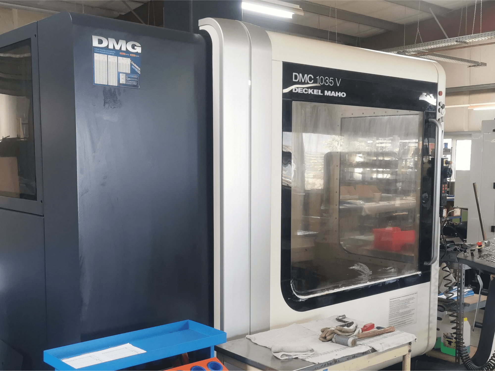 DMG DMC 1035 V freesmachine in een werkplaats, vooraanzicht met blauwe gereedschapsbak en handschoenen op het oppervlak.
