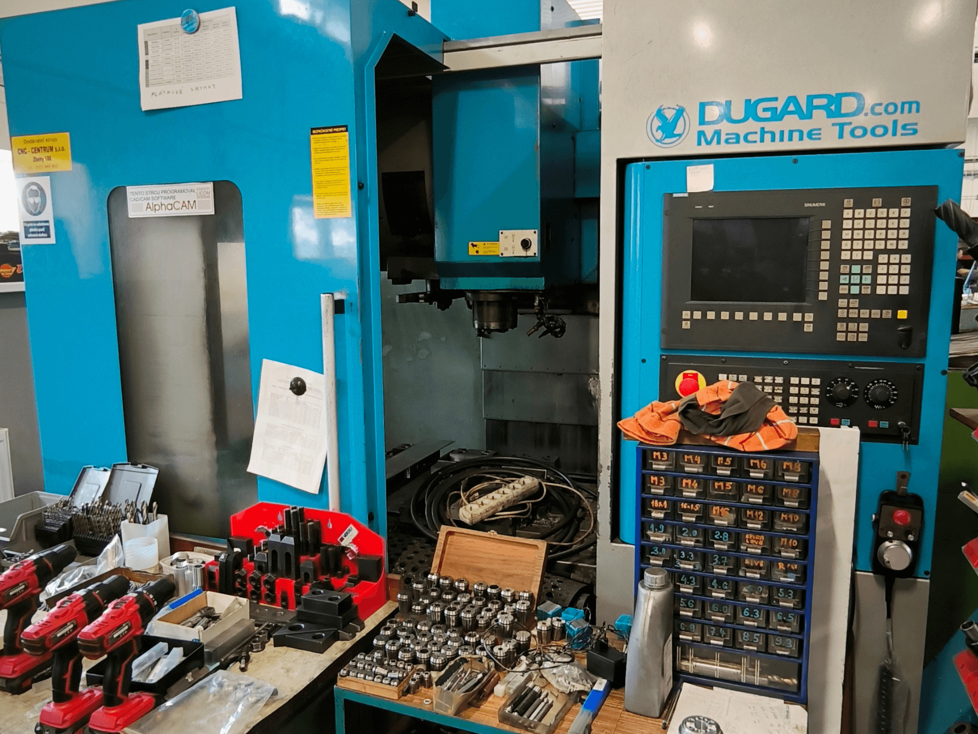 Vooraanzicht van Dugard 850VMC verticaal bewerkingscentrum, met bedieningspaneel, gereedschappen en accessoires op een werkbank.