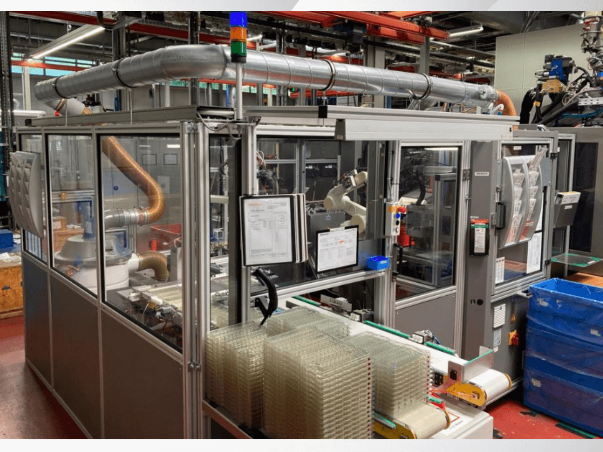 Geautomatiseerde assemblagemachine met robotarm, transparante zijpanelen en gestapelde containers met heldere items, vooraanzicht.