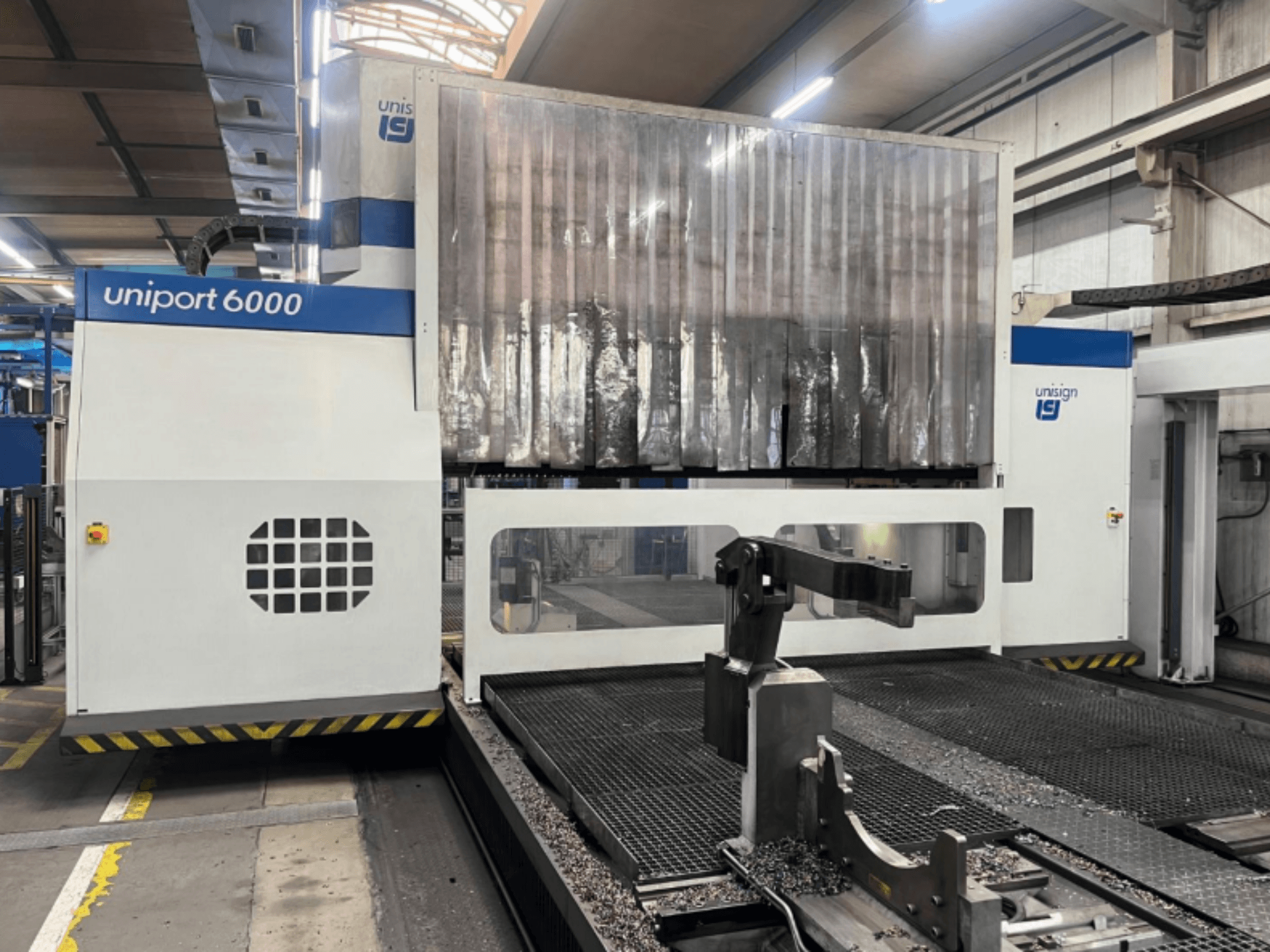 Portaalfreesmachine Unisign uniport 6000, vooraanzicht, waarop de machinestructuur en het snijgedeelte met metaalschilfers te zien zijn.