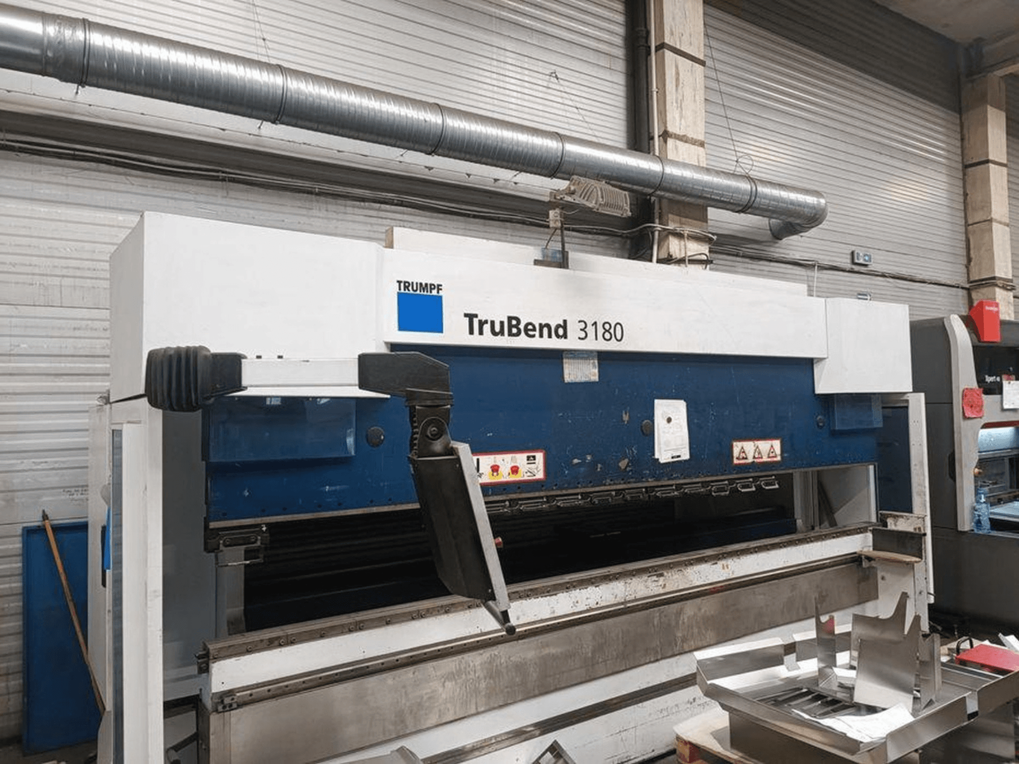 Trumpf TruBend 3180 buigmachine in een werkplaats, zijaanzicht met bedieningspaneel en metalen stukken op de tafel.