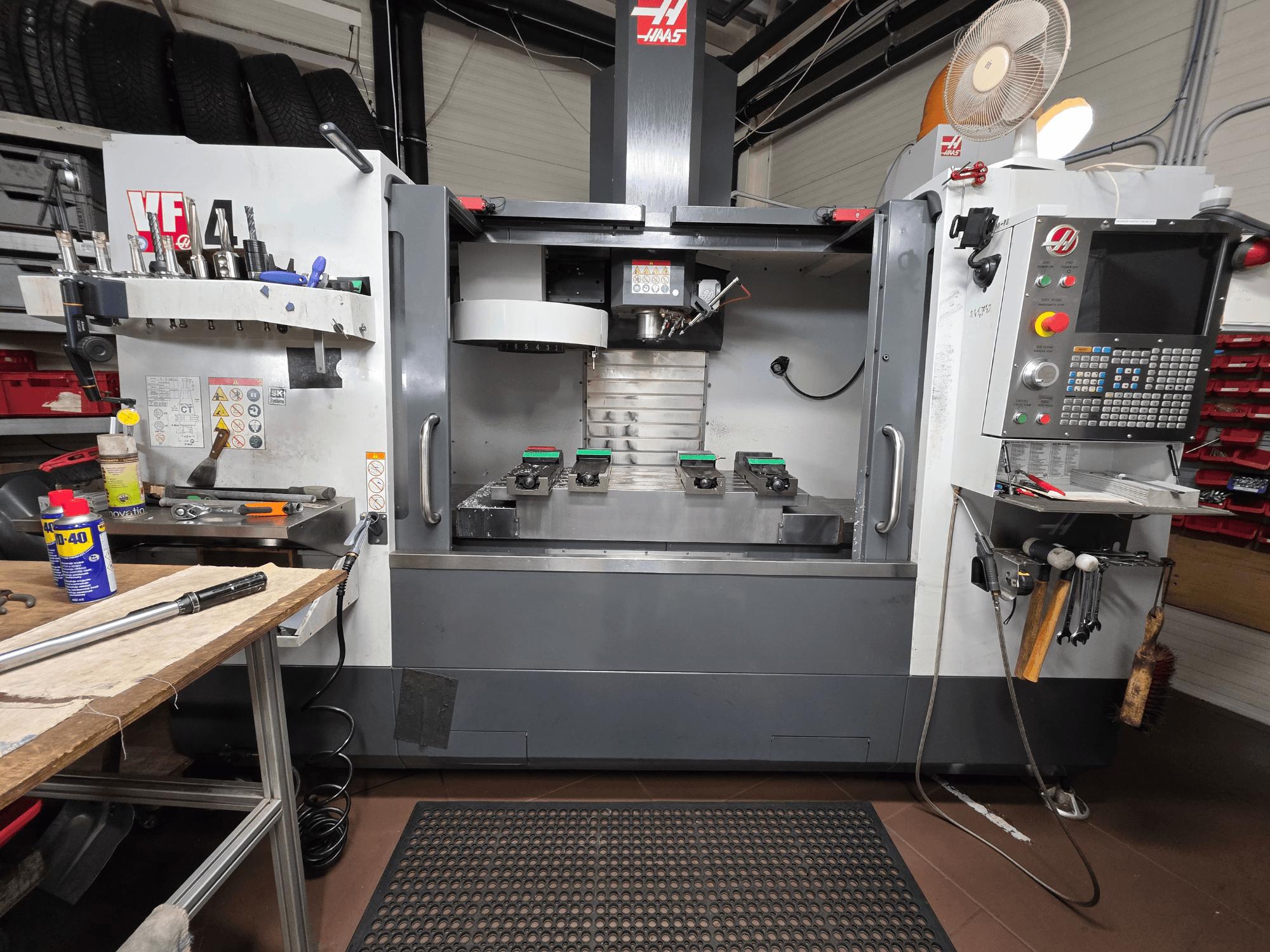 Vooraanzicht van de Haas VF-4 CNC-frees in een werkplaats, met gereedschappen, een computerinterface en twee werkstukken op de tafel.