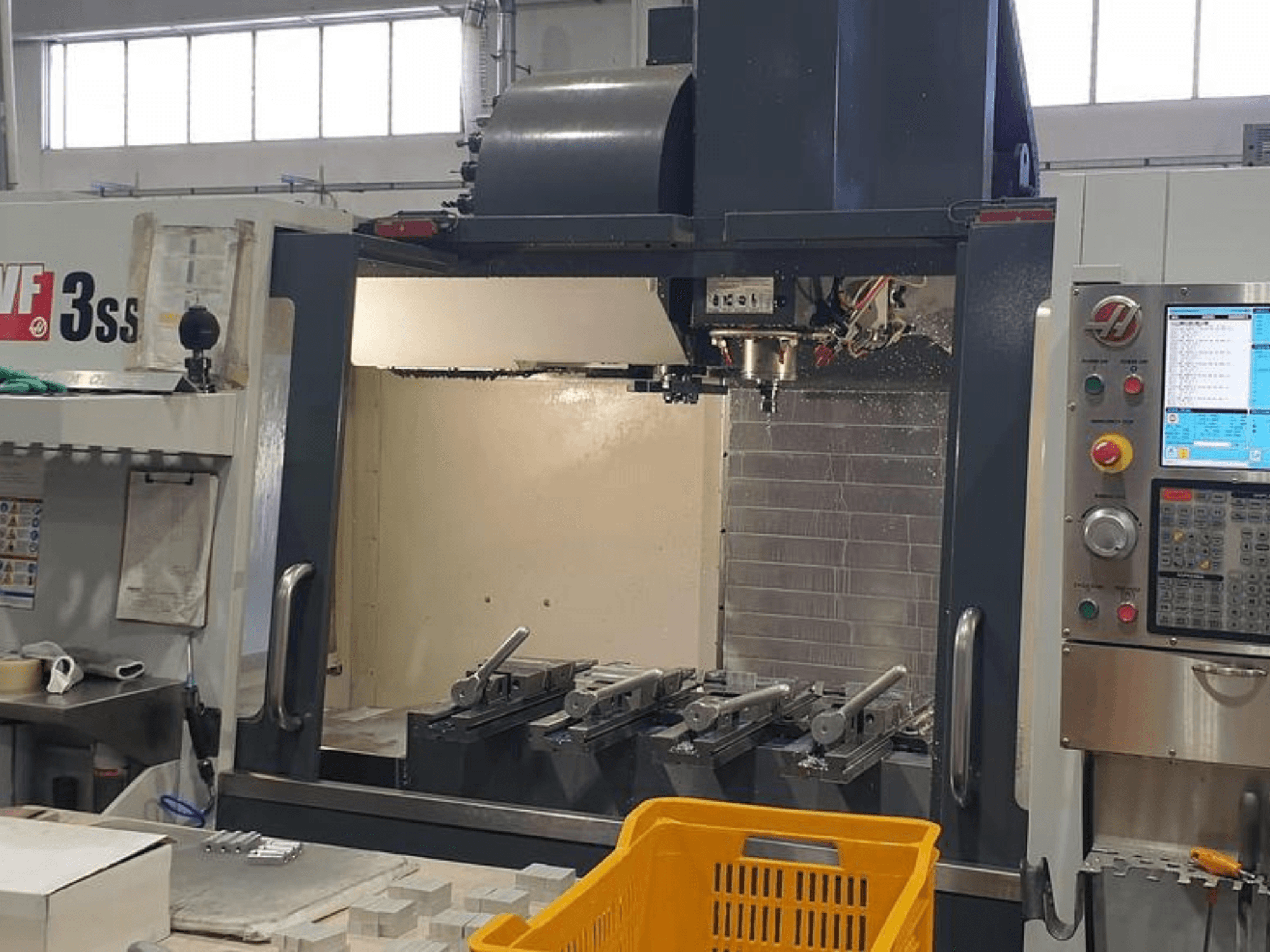 HAAS VF-3SS verticaal bewerkingscentrum, vooraanzicht met CNC-bedieningspaneel, gereedschappen en oranje mand.