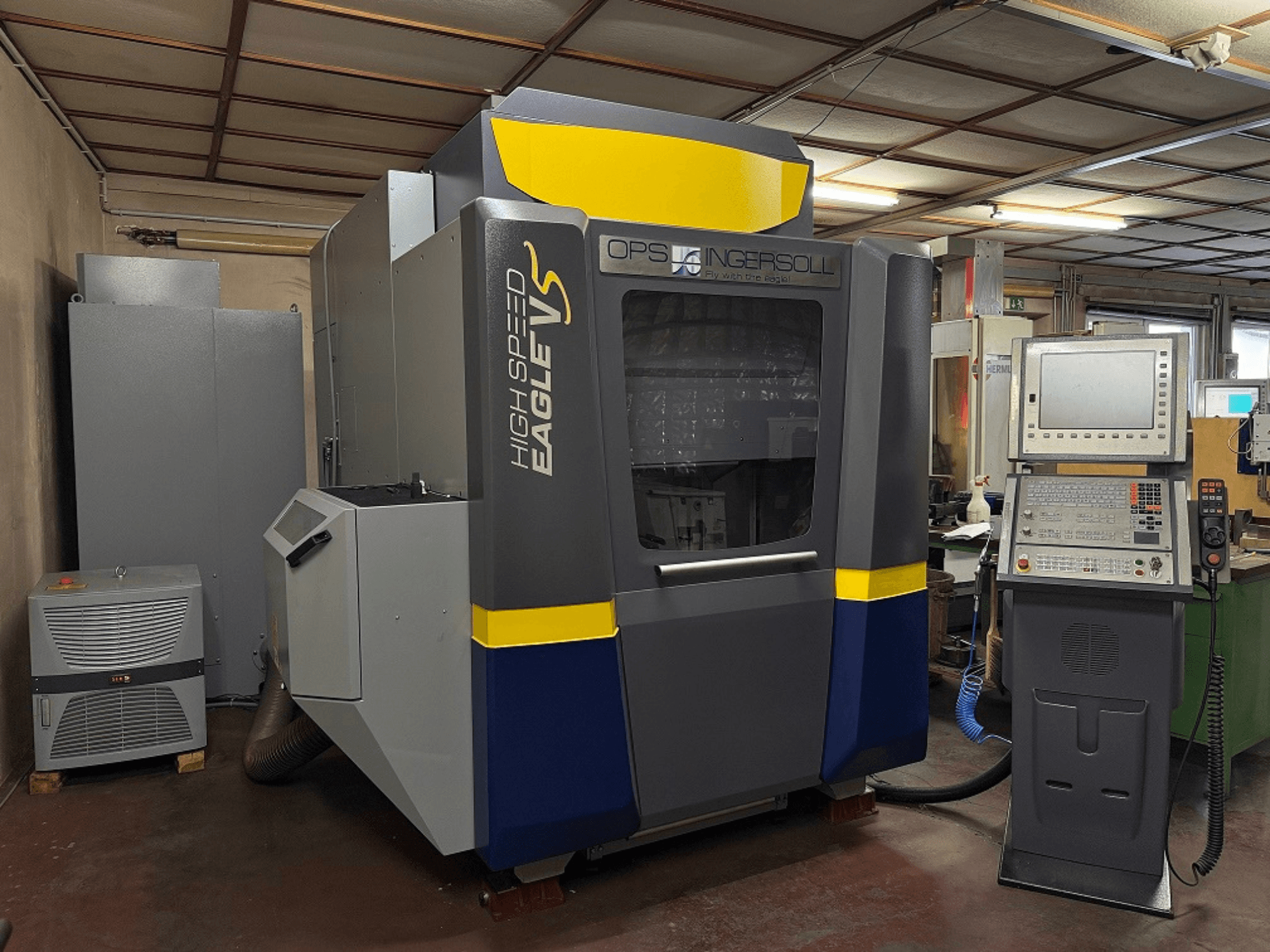 High Speed Eagle V machine van OPS Ingersoll, zijaanzicht, met bedieningspaneel en aangrenzende apparatuur in een industriële omgeving.