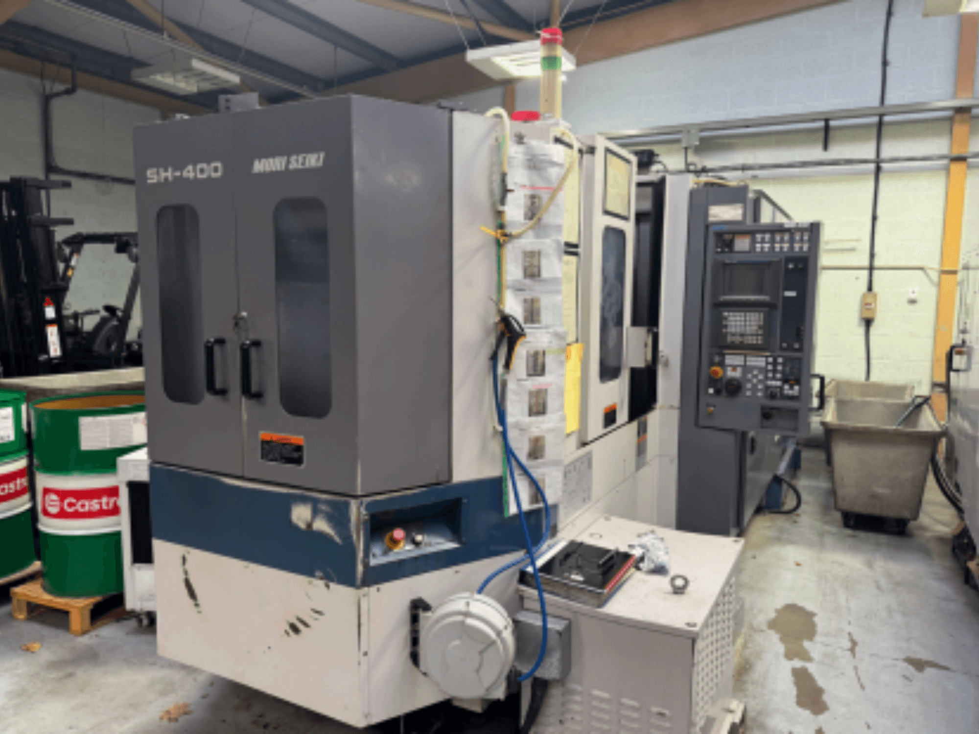 Moni Seiki SH-400 CNC machine, zijaanzicht met bedieningspaneel, deuren en omringende industriële omgeving.