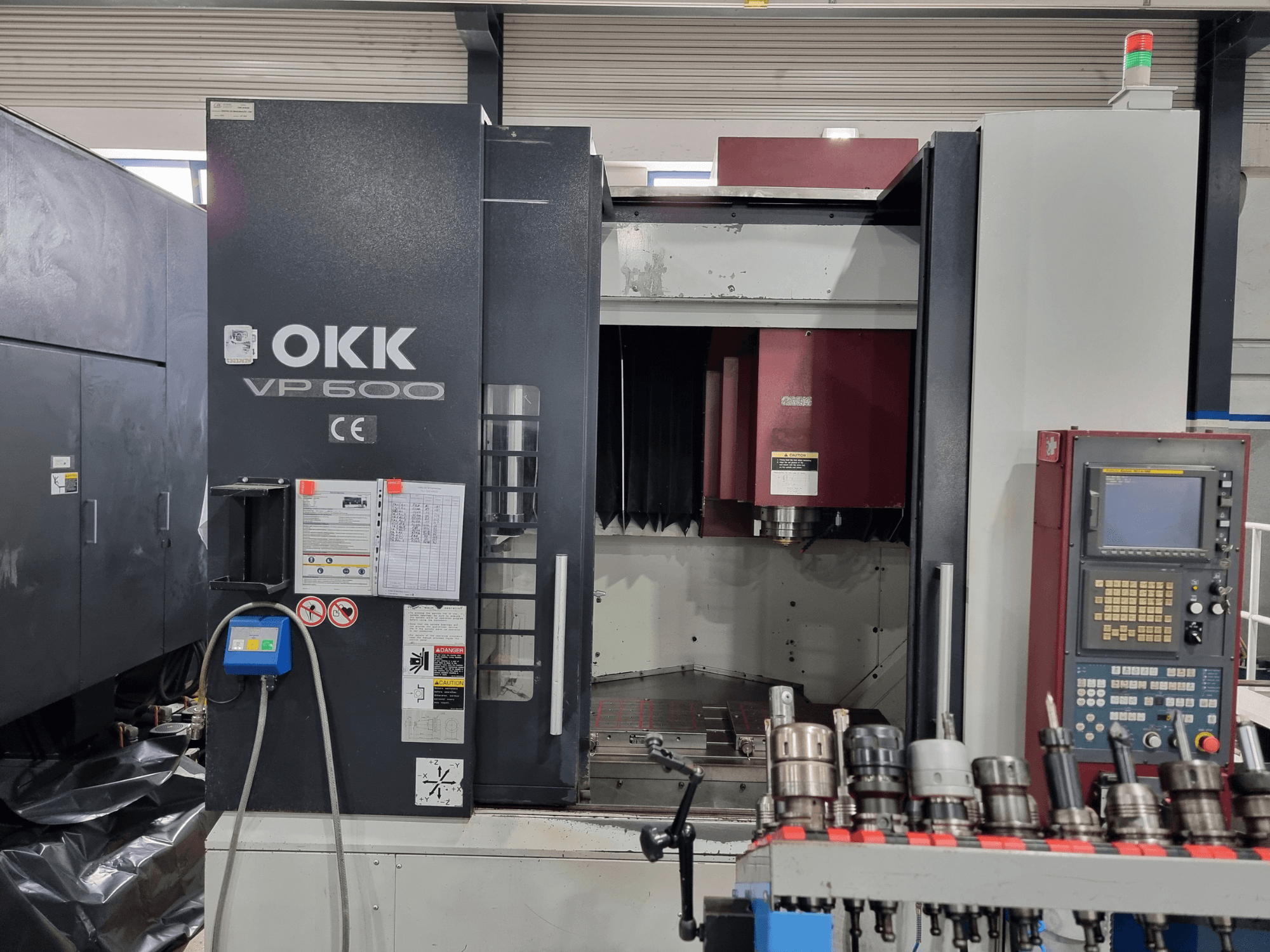 Het verticale bewerkingscentrum OKK VP600 gezien vanaf de voorkant, met het bedieningspaneel en de gereedschapshouders op een rek.