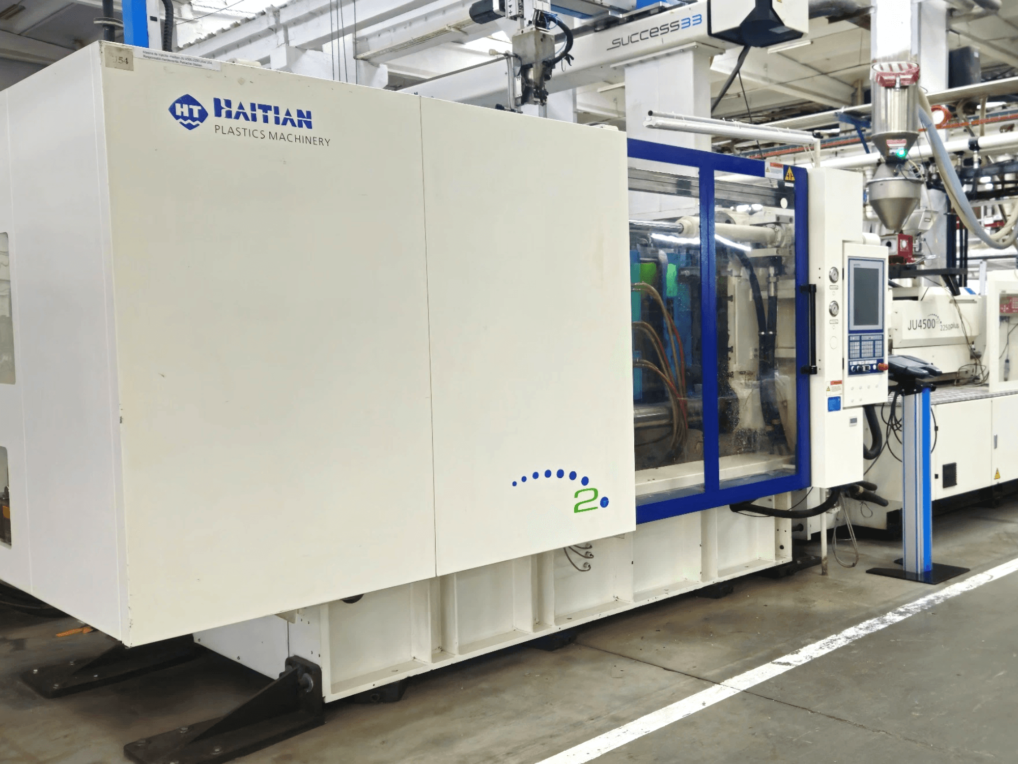 Maquette van Haïtiaanse kunststofmachines, vooraanzicht, met machines met bedieningspaneel en zichtbare leidingen, in een industriële omgeving.