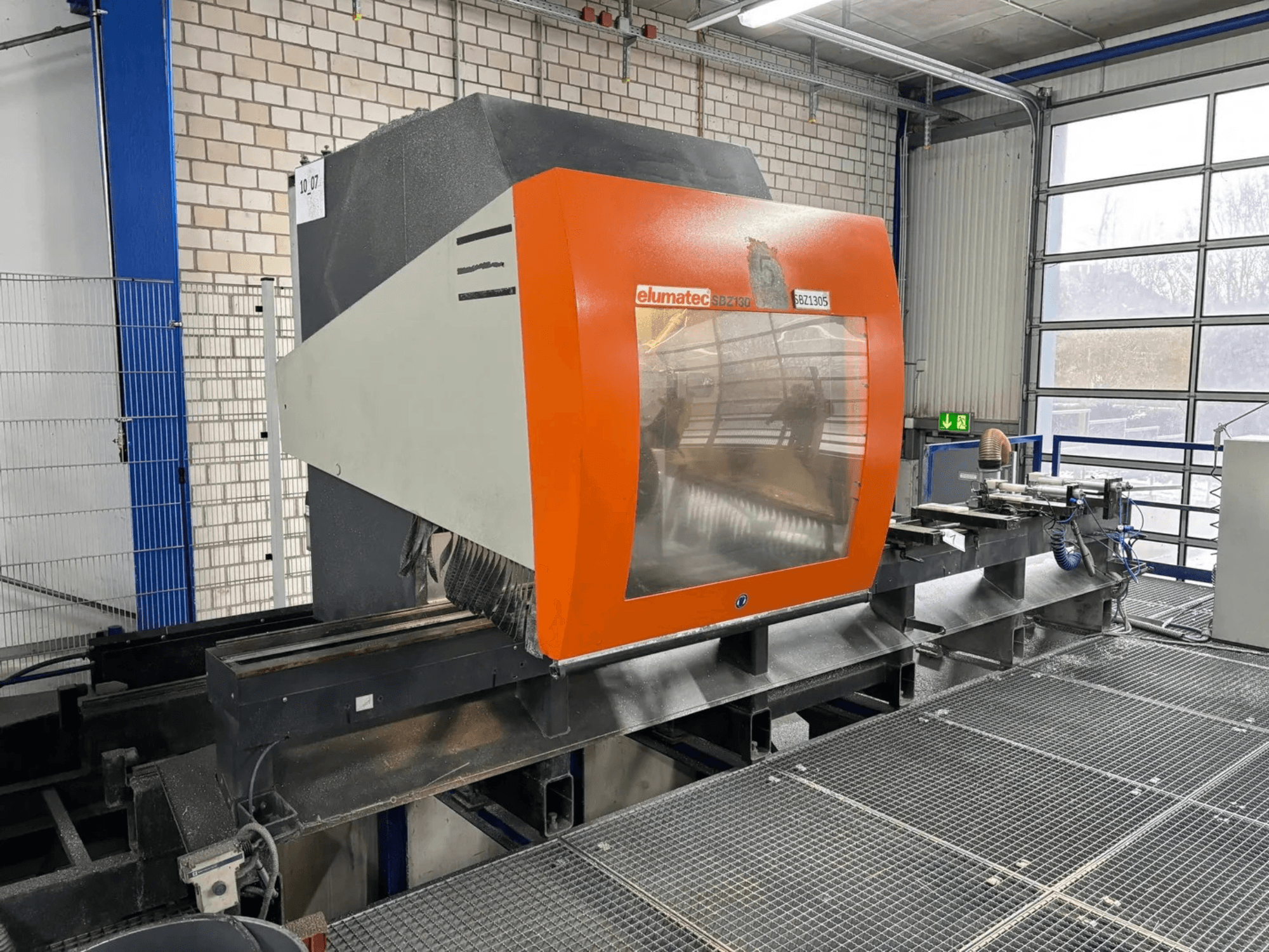 Elumatec SBZ 130 verticaal bewerkingscentrum, vooraanzicht, met een oranje en grijze behuizing met een transparant paneel.