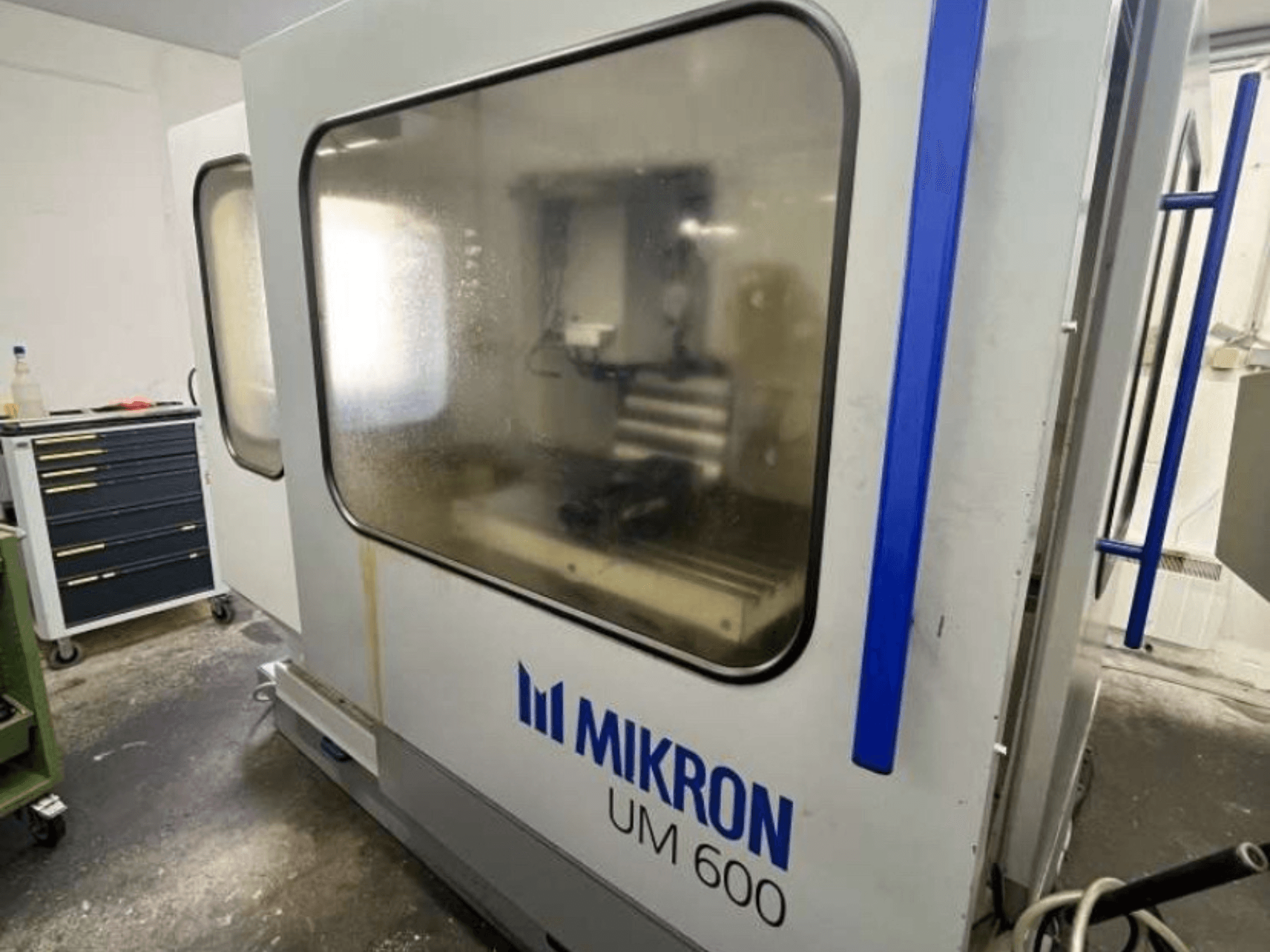 MIKRON UM 600 TNC 410/426 universeel bewerkingscentrum, zijaanzicht, met beslagen glas en zichtbare gereedschapsopberging in de buurt.