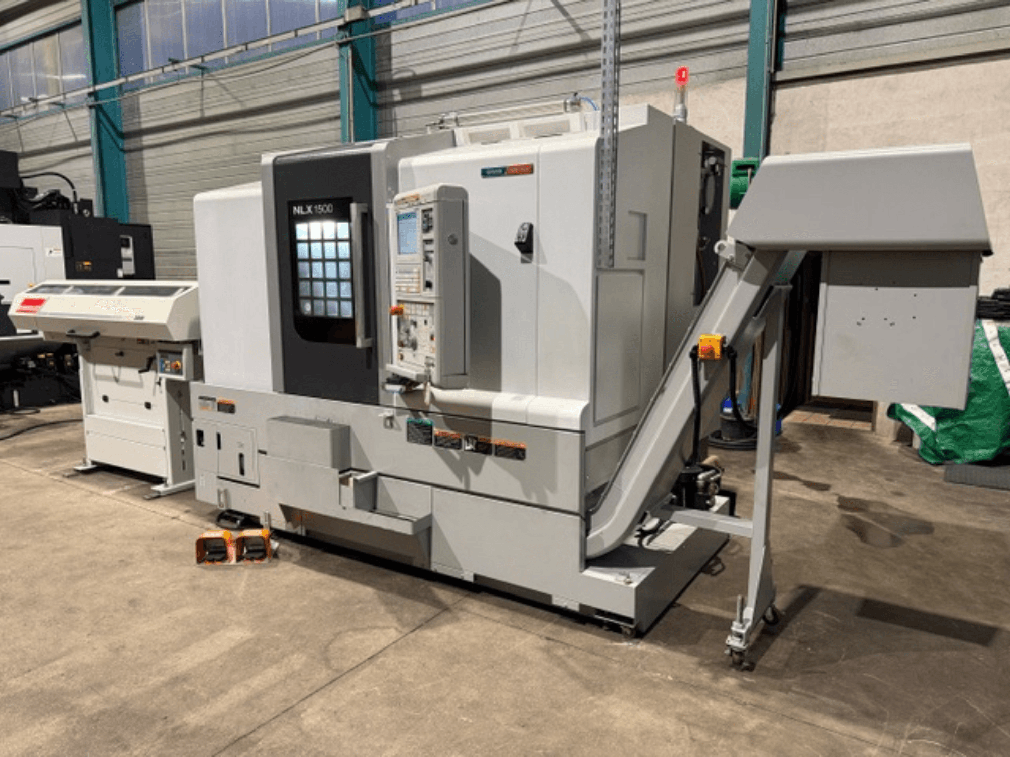 NLK 1500 CNC machine, vooraanzicht, met bedieningspaneel en trechter voor accessoires aan de zijkant, rustend op betonnen vloer.