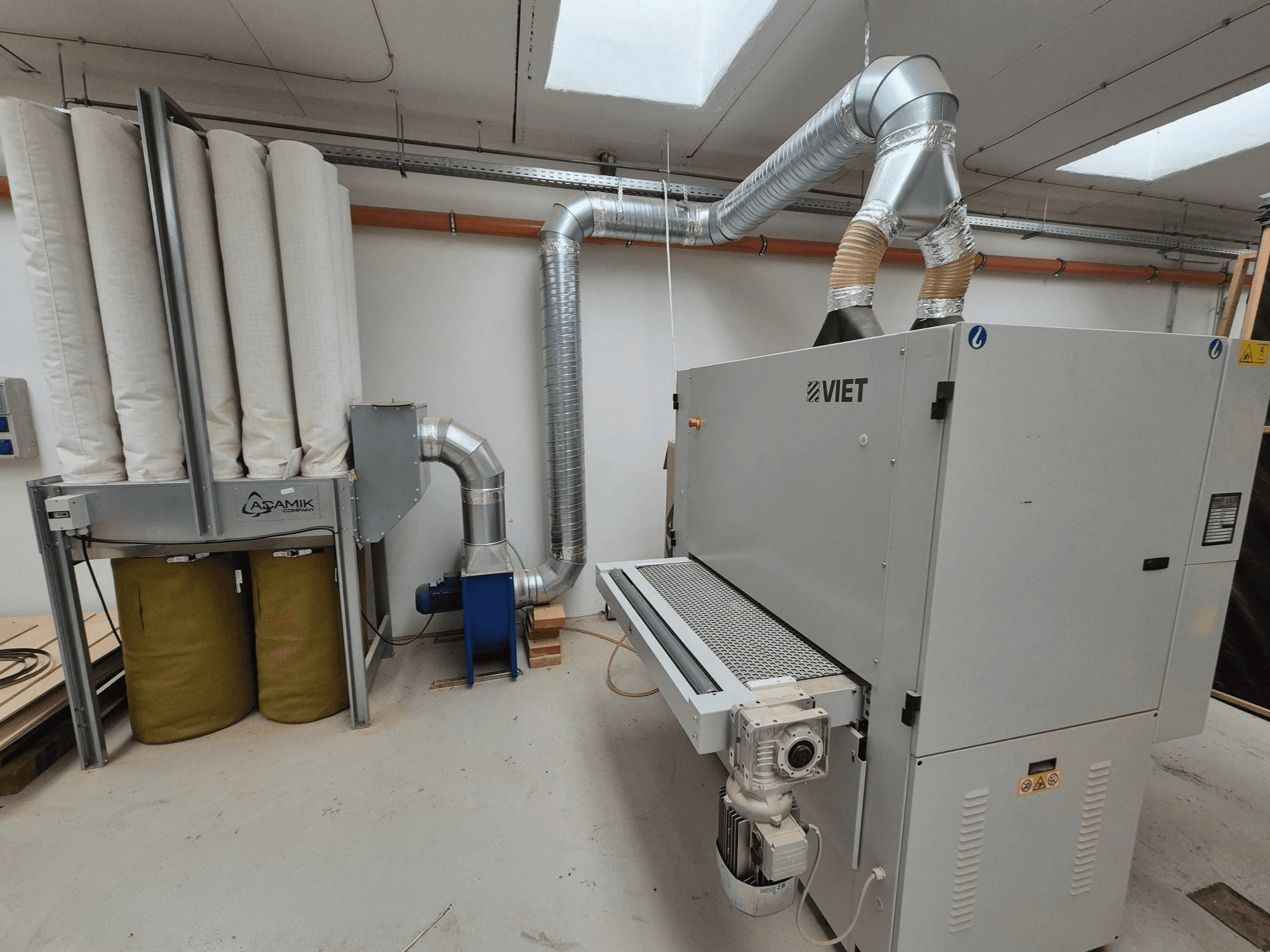 Viet stofafzuigsysteem met cilindrische filters en een zilveren uitlaat, gezien vanaf de voorkant in een werkplaats.