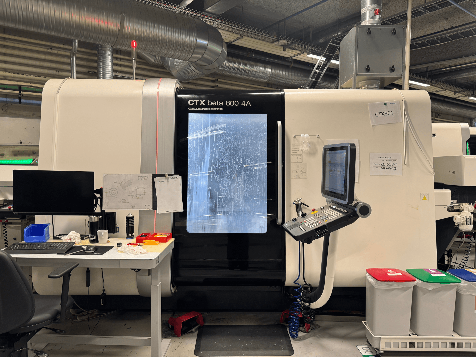 CTX beta 800 4A machine met bedieningspaneel en monitor, zijaanzicht, in een werkplaats met kantooropstelling en gekleurde afvalbakken.