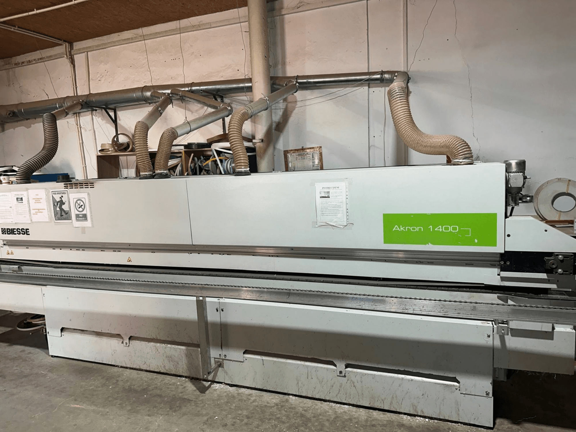 Een BIESSE Akron 1440 A kantenlijmmachine in zijaanzicht, met afzuigkanalen, bedieningspaneel en gebruiksstickers.