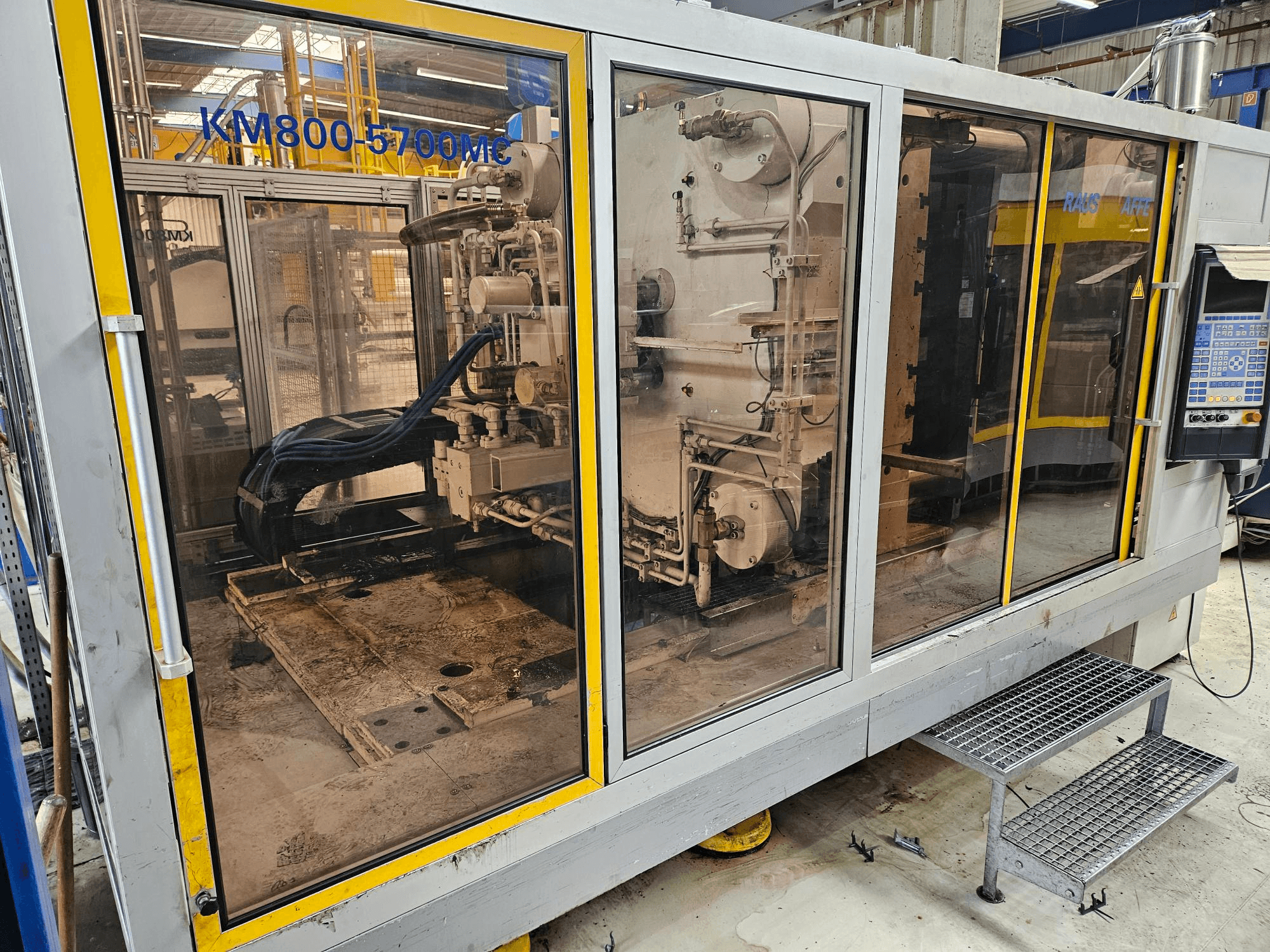 Hydraulische spuitgietmachine Krauss Maffei KM800-5700 MC, vooraanzicht met zicht op de onderdelen door de glazen panelen.